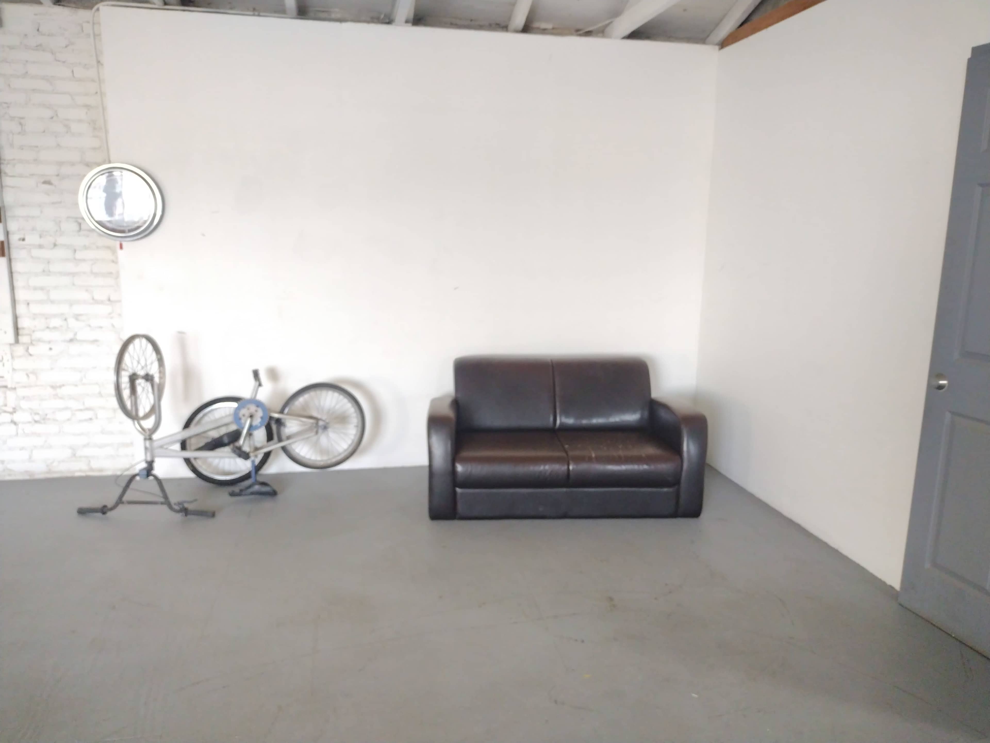 A brown couch positioned against a white wall, with a bicycle resting on its side nearby.