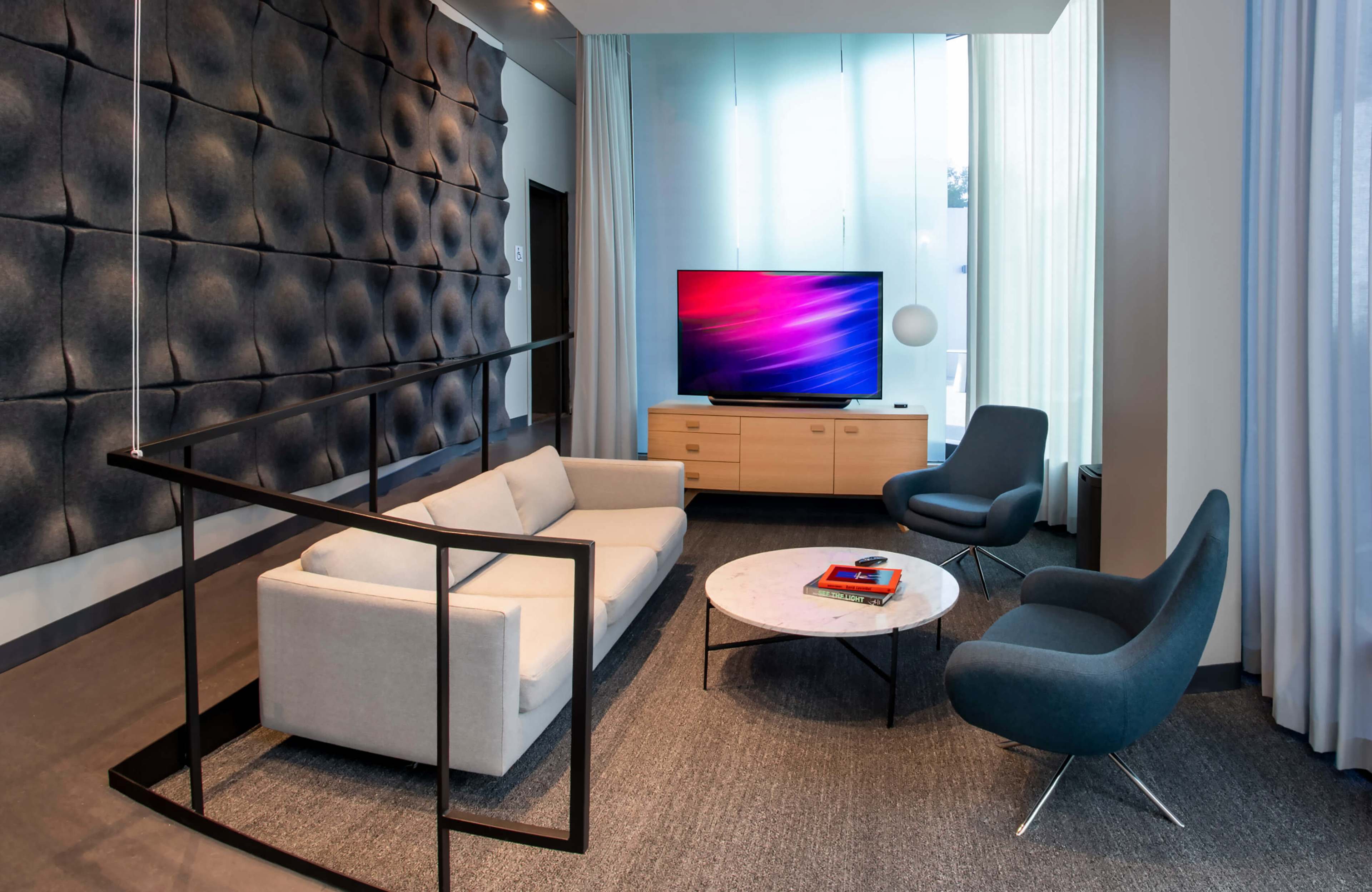 A modern living room features a gray sofa, blue armchair, a marble coffee table, and a wall-mounted television above a light wooden cabinet.