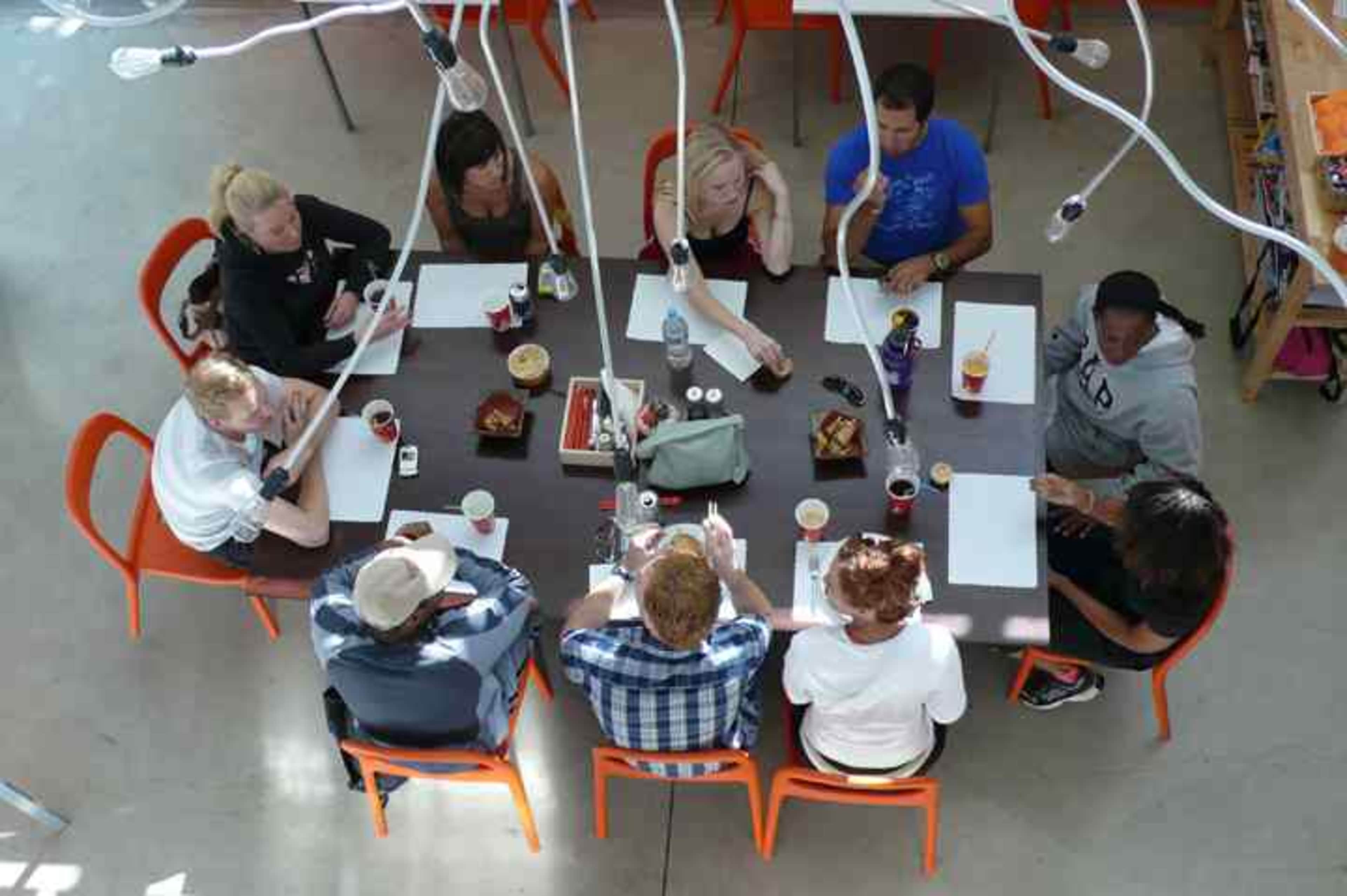 A group of ten people sits around a table in a bright, modern space, engaged in discussion while taking notes and enjoying beverages.