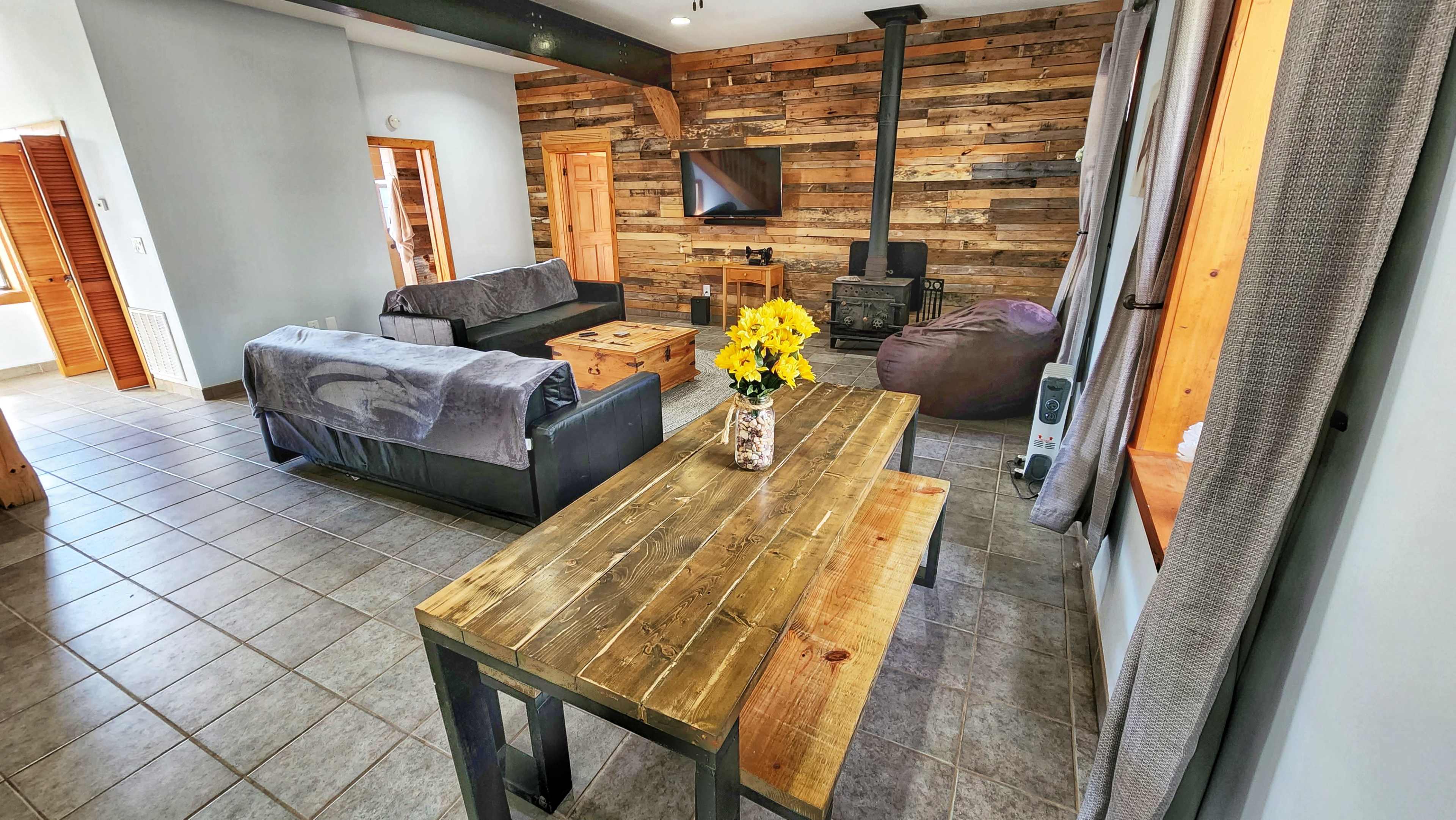 A living room with a wooden accent wall, a television mounted on it, a coffee table, two sofas, and a dining table with a vase of flowers.