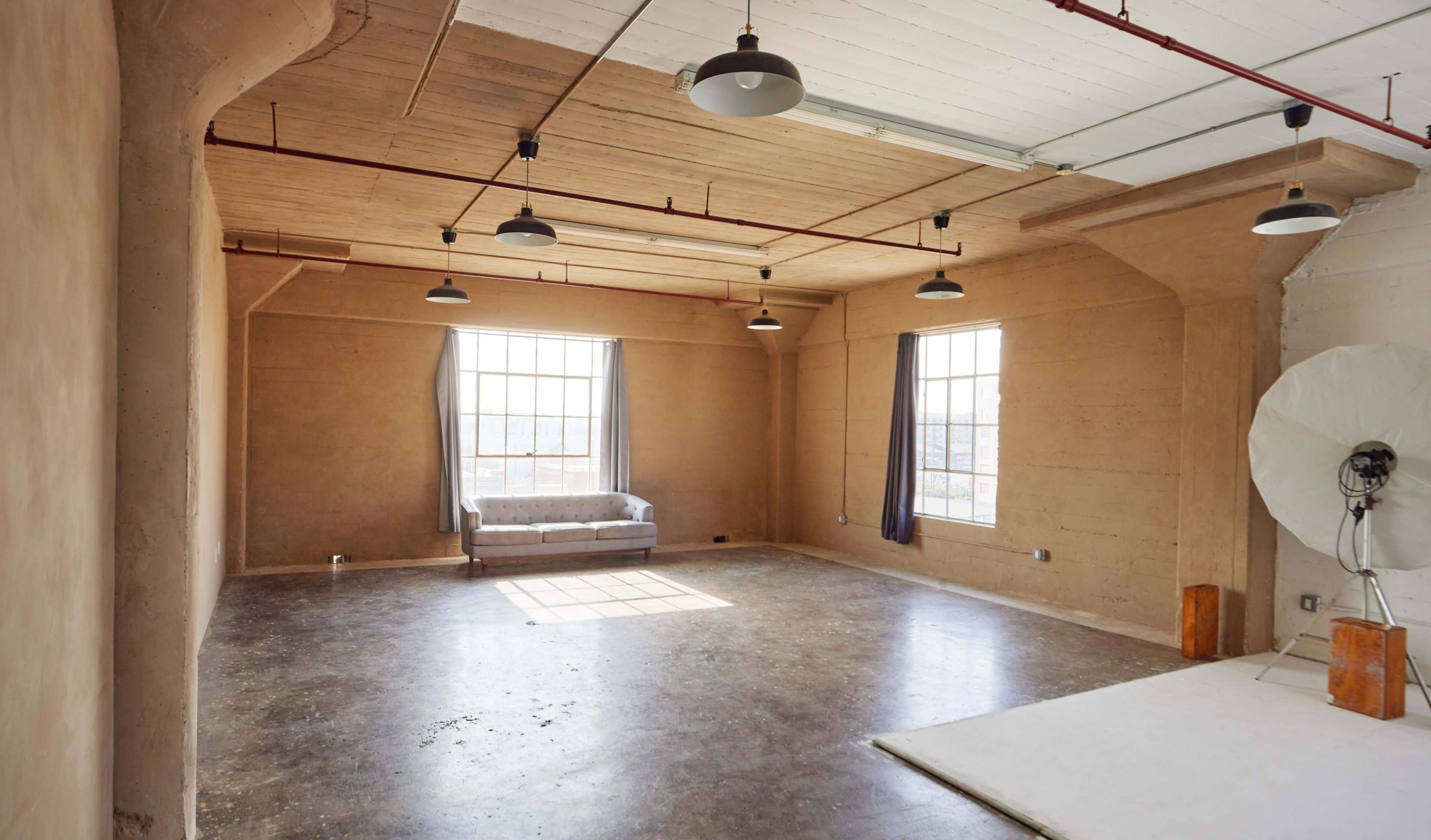 A spacious, minimalist room with a concrete floor, large windows, and a gray couch against the wall.