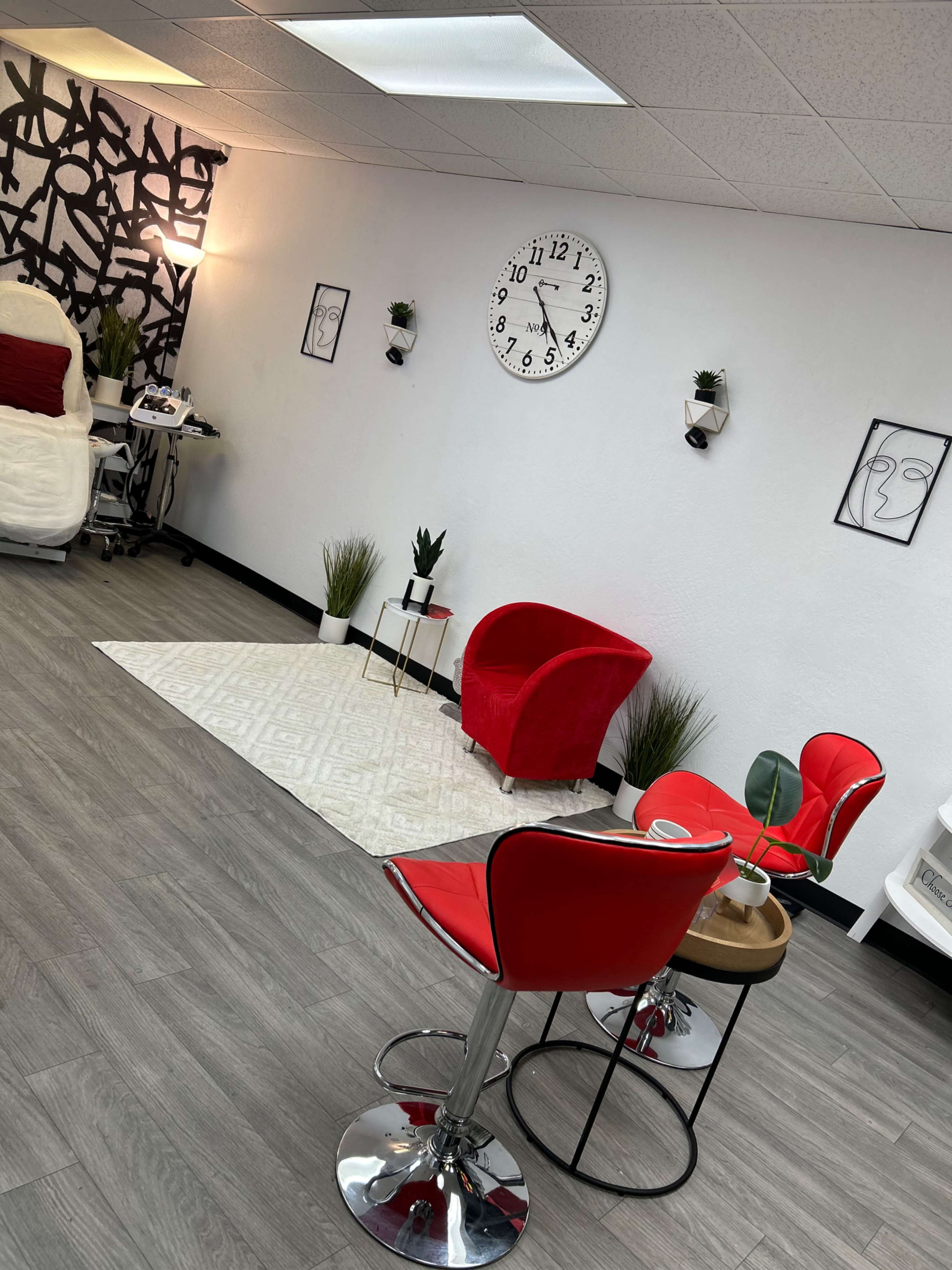 A modern interior space featuring red chairs, a round wooden table, a large wall clock, and minimalist decor with plants and artwork.