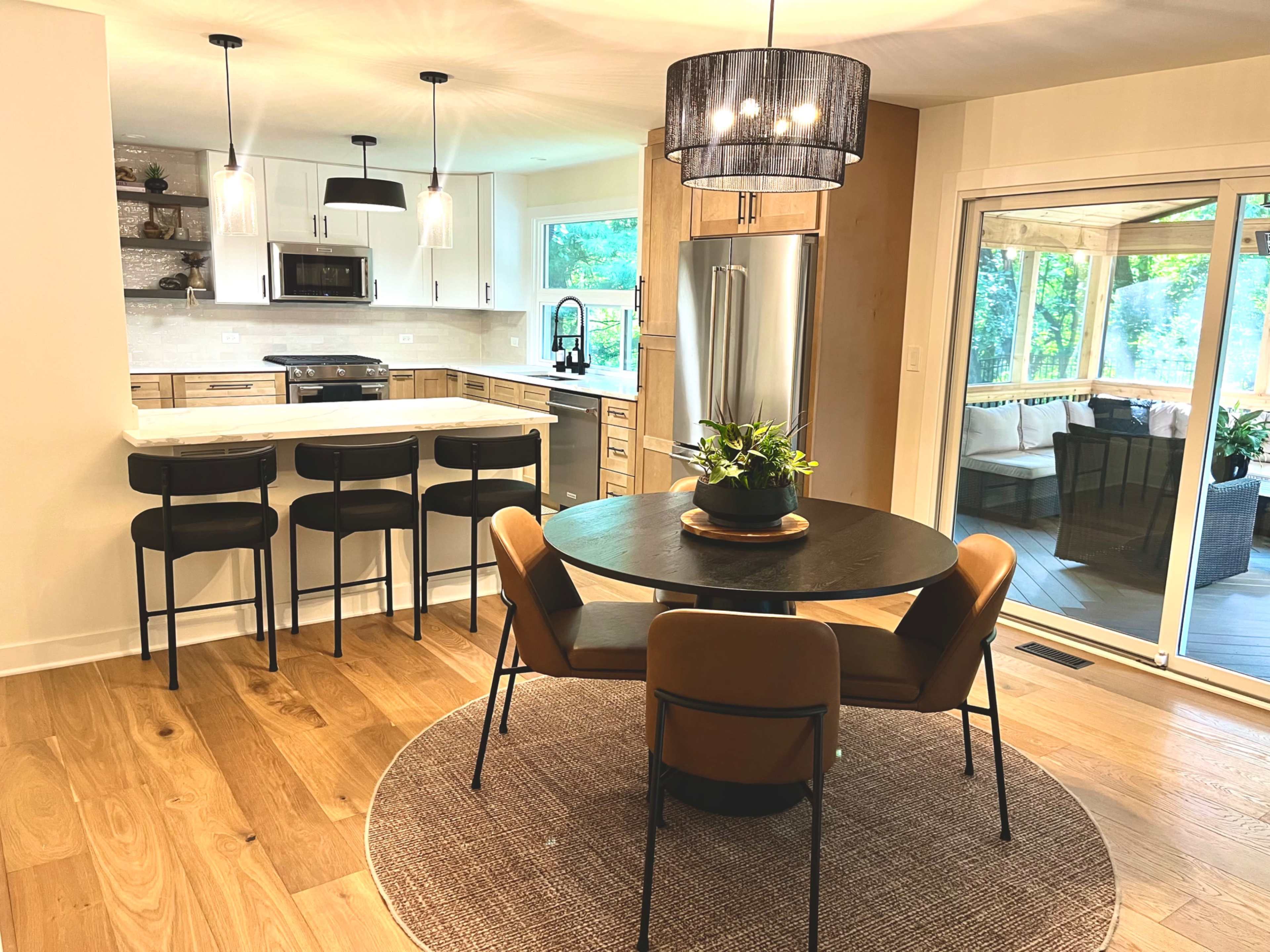 A modern kitchen and dining area features a round table with four chairs, a large island with bar stools, and sliding glass doors leading to a patio.