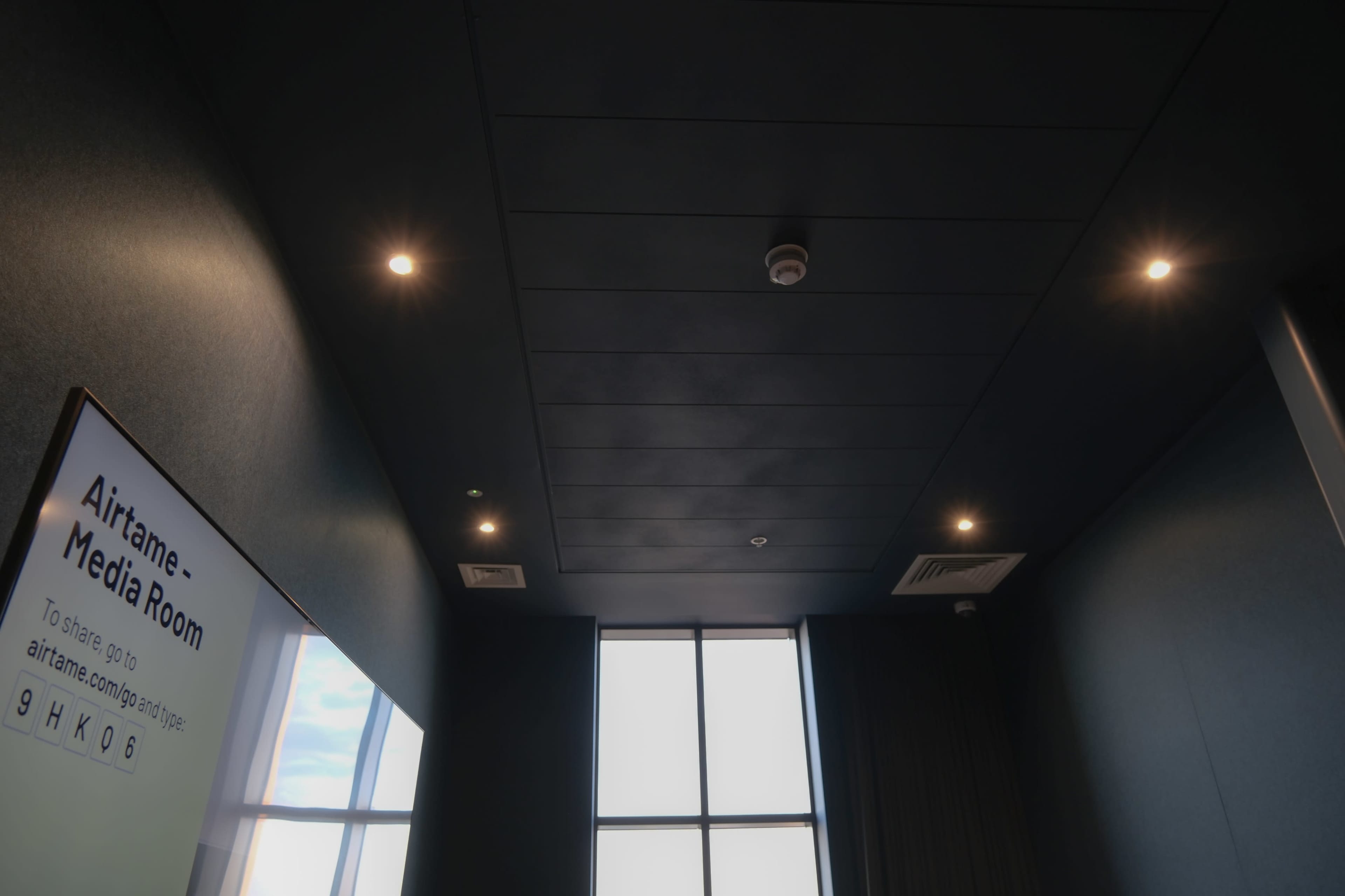 A dark ceiling with recessed lights and a large window revealing the sky outside.