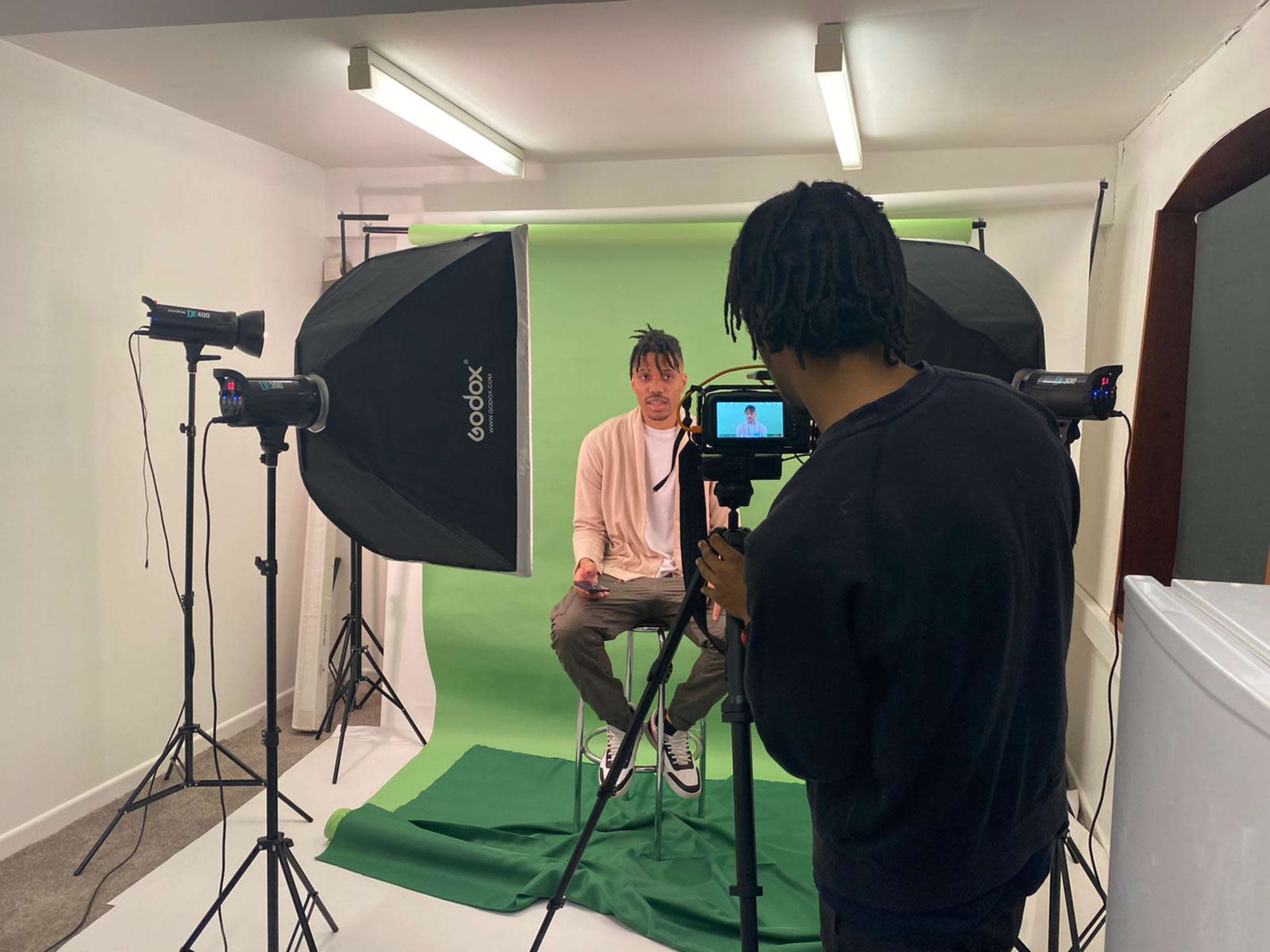 A person is being filmed in front of a green backdrop with studio lighting in a photography setup.