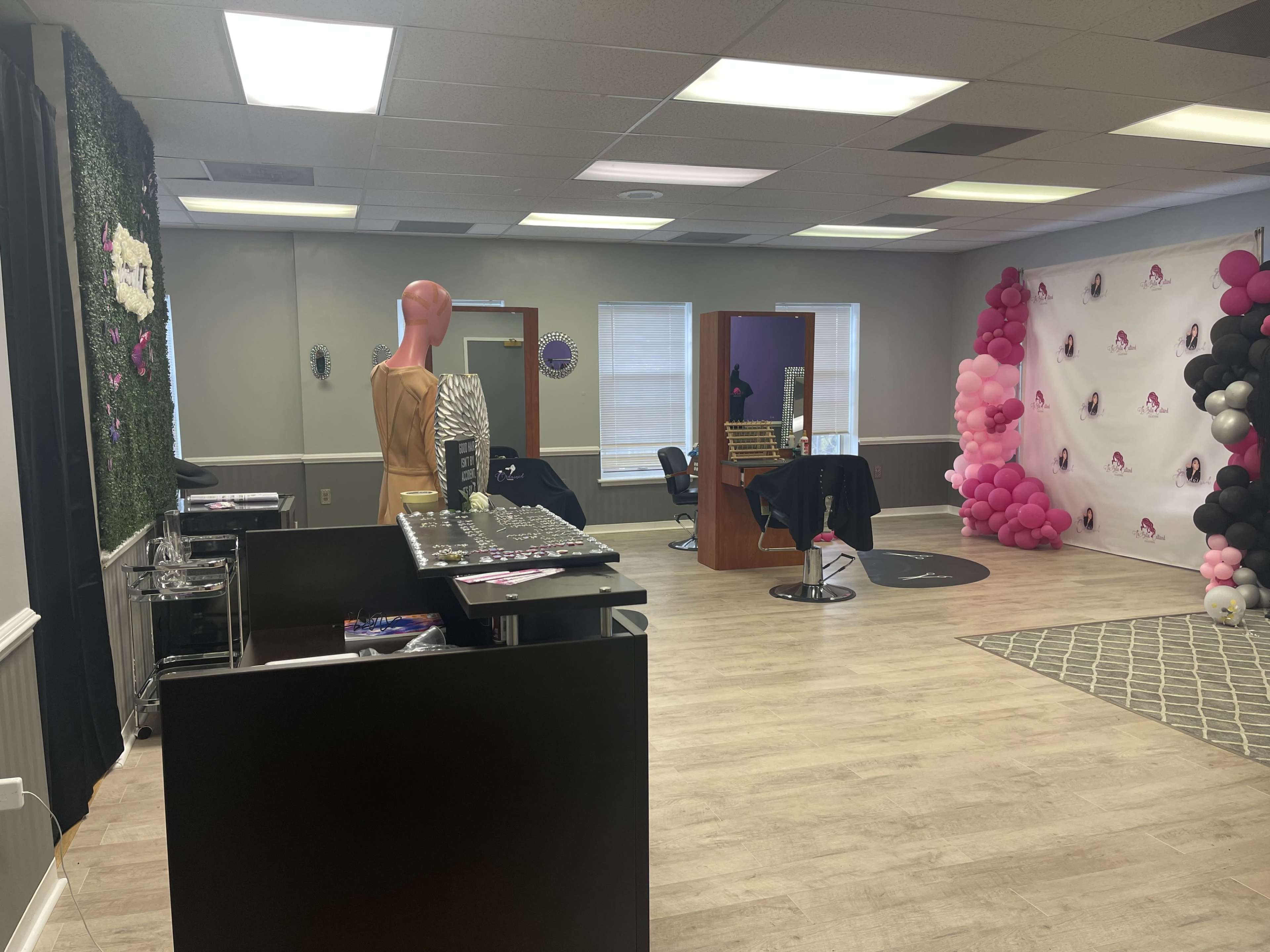 A salon interior featuring a reception area with a mannequin, a decorated wall with balloons, and salon stations in the background.