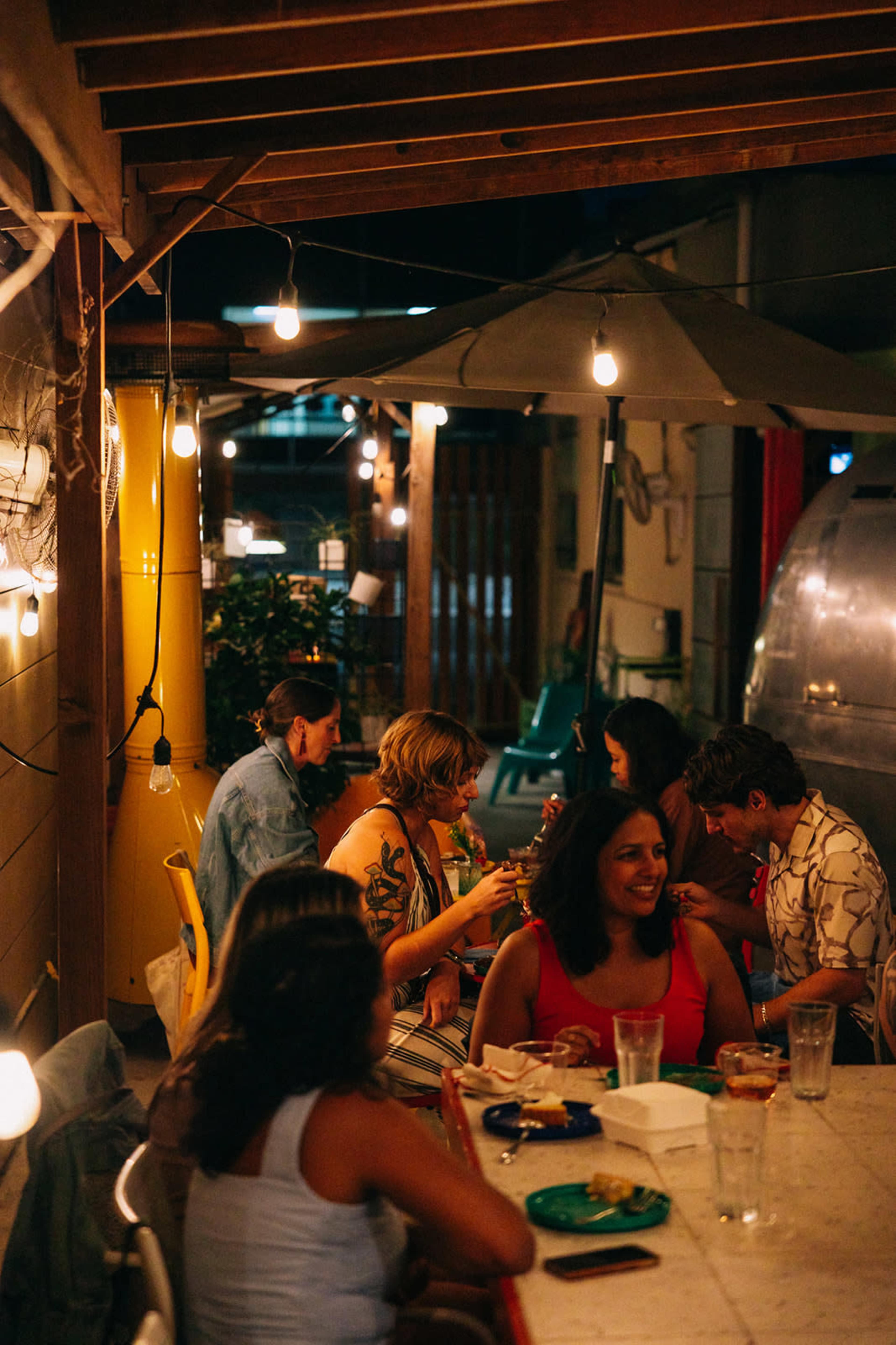 A group of people sits at a table in a dimly lit outdoor dining area adorned with string lights.