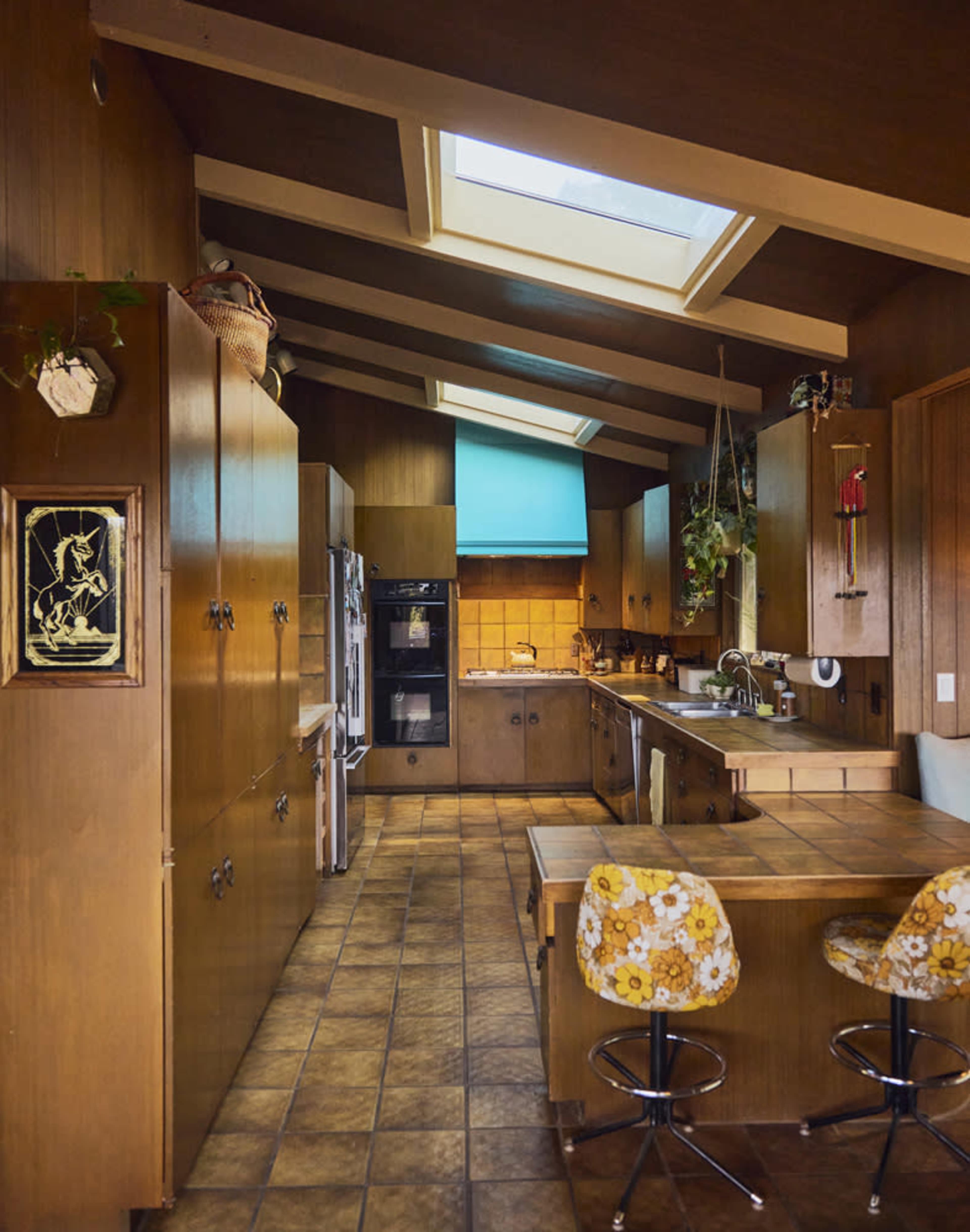 A kitchen with wooden cabinetry, tiled flooring, and skylights illuminating the space, featuring a central dining area with patterned bar stools.