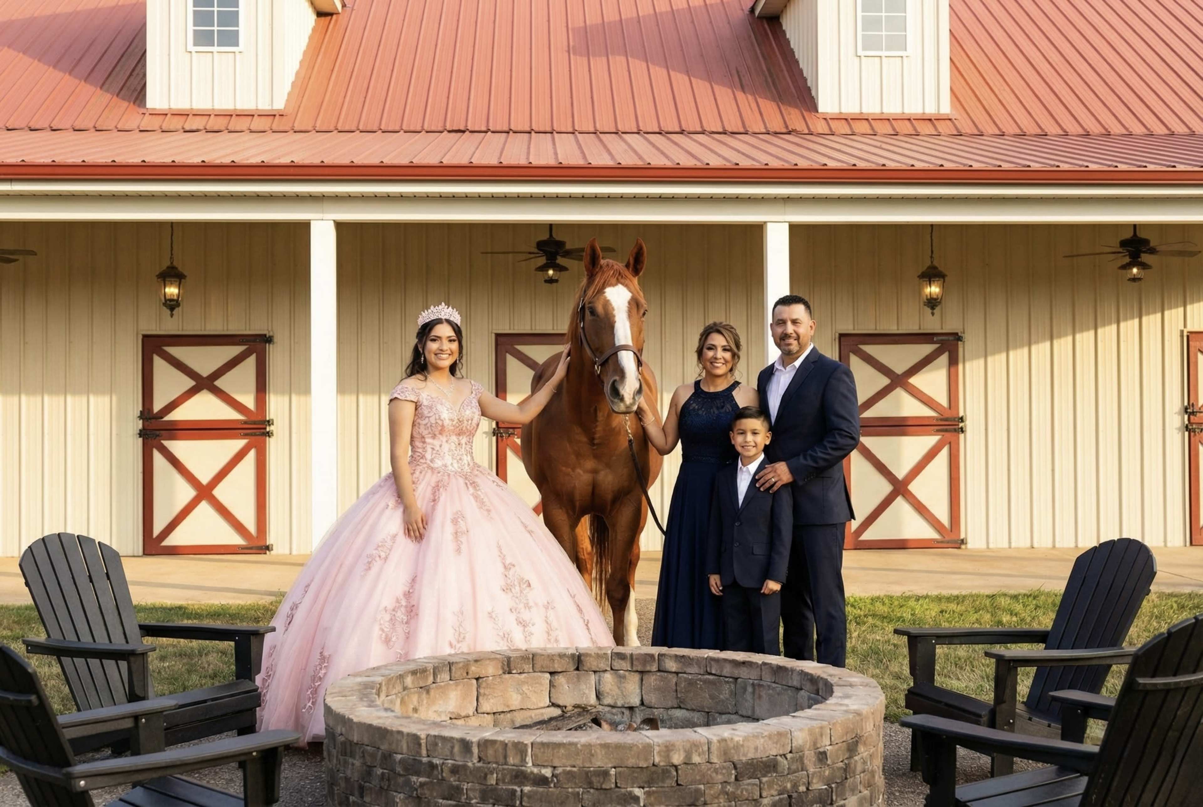 A young girl in a long pink dress stands beside a horse, while two women and a boy pose together in front of a barn with red doors.