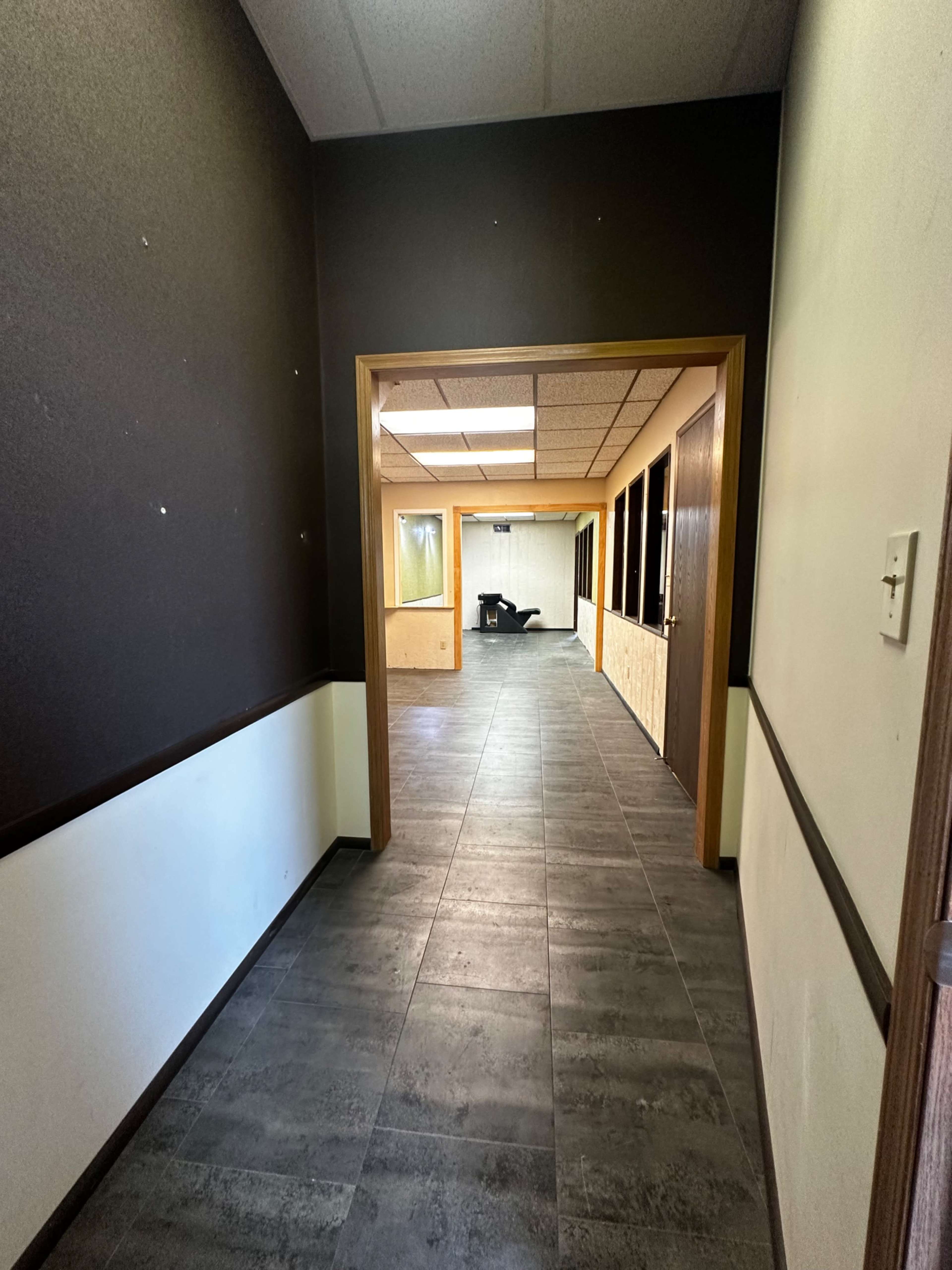 The image shows a hallway leading to a room with several doors on the right and a visible area at the end.