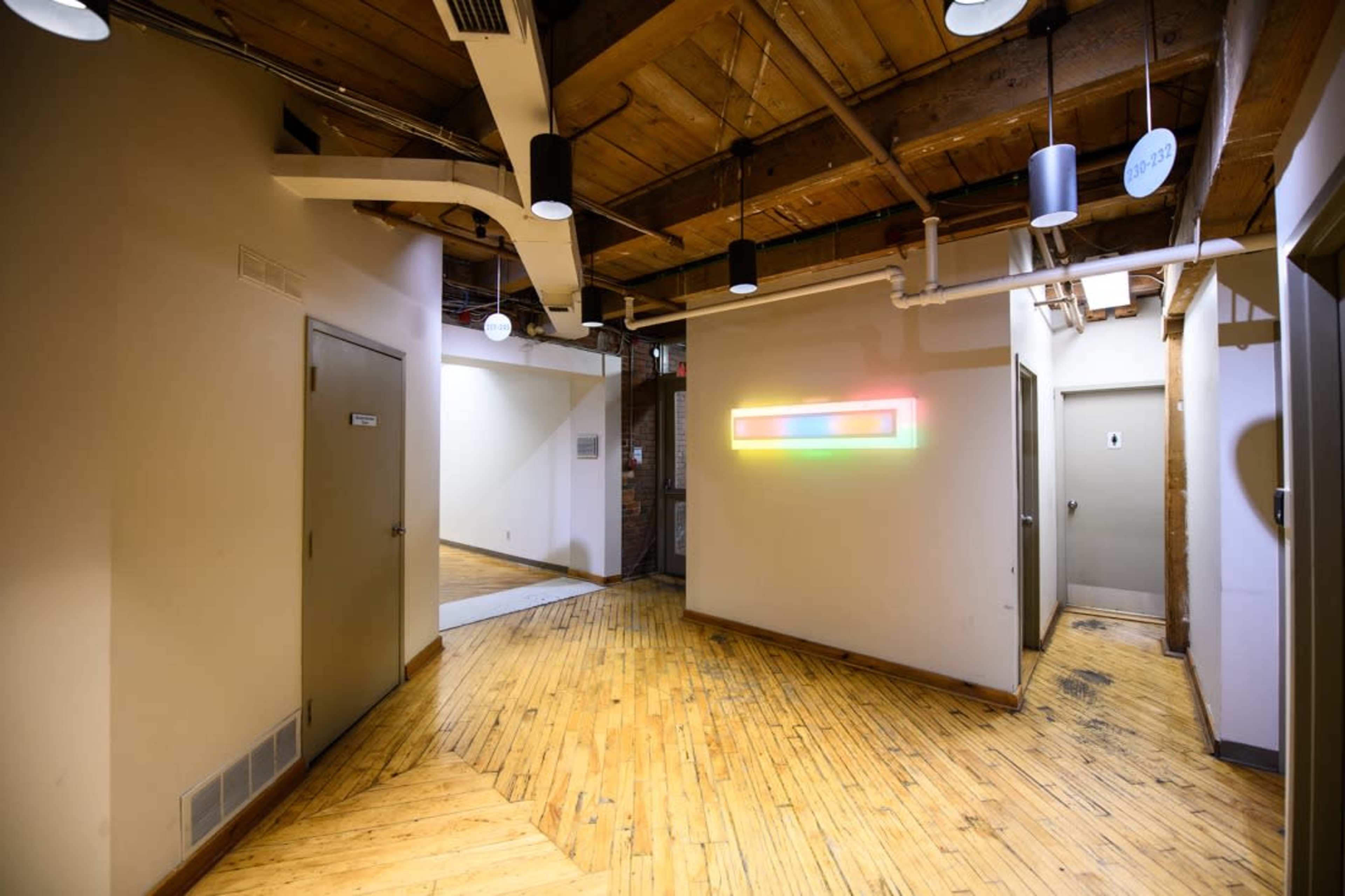 A modern hallway with wooden flooring, featuring doors leading to rooms and a colorful LED light installation on the wall.