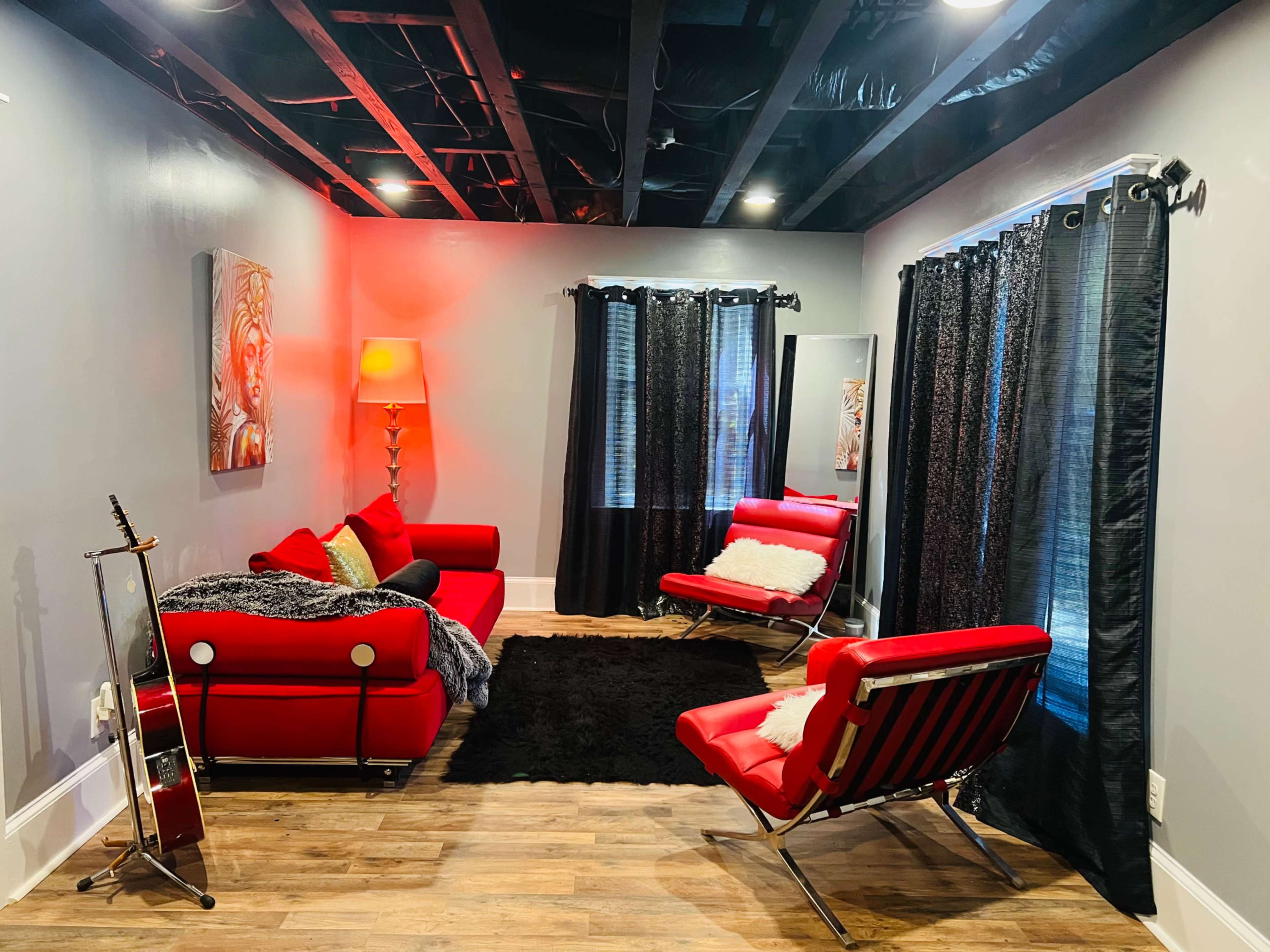 The image shows a modern living room with red furniture, including a sofa and chairs, black curtains, and a wooden floor.