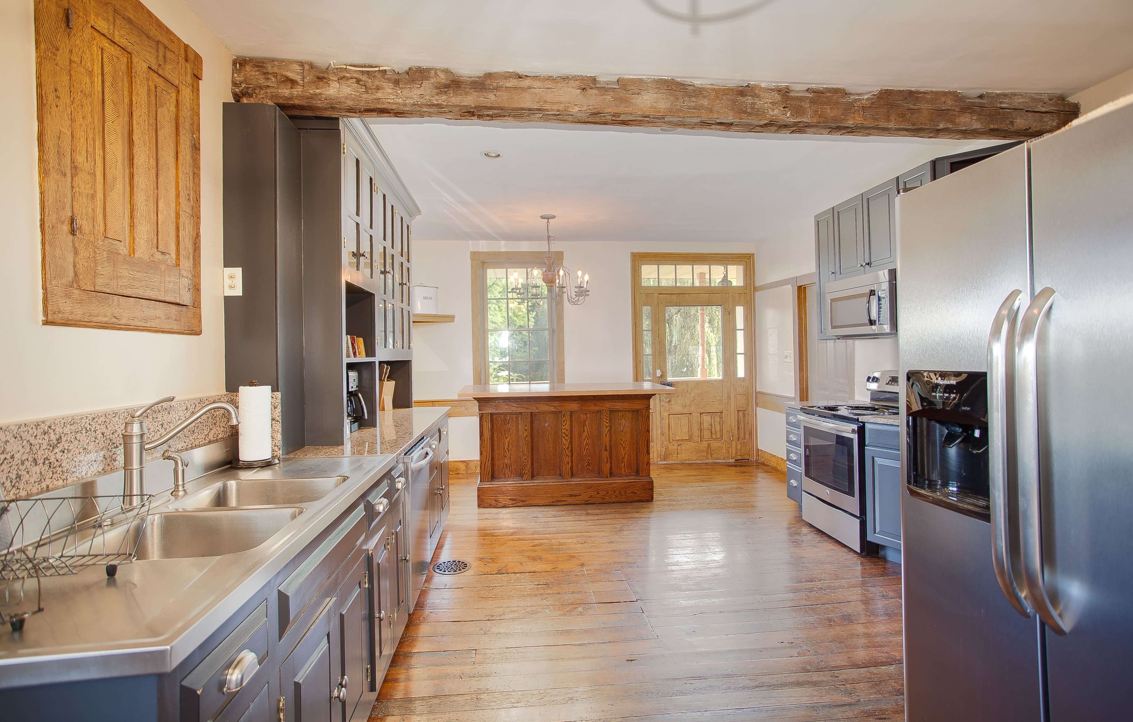 A kitchen featuring stainless steel appliances, gray cabinets, a wooden beam overhead, and a bar area with a door leading outside.
