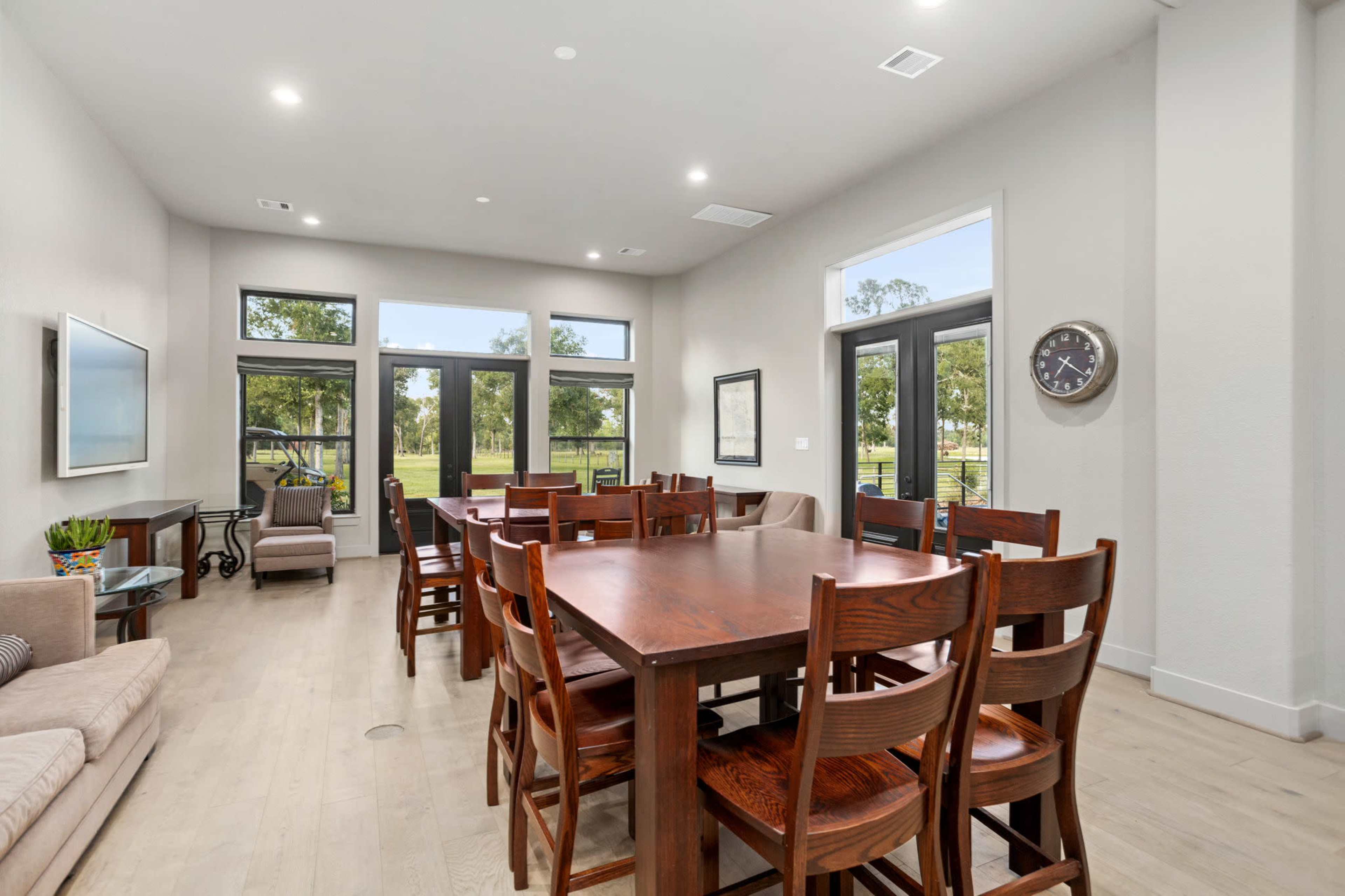 A spacious, well-lit dining area with a large wooden table surrounded by chairs, adjacent to a living space featuring a sofa and large windows.