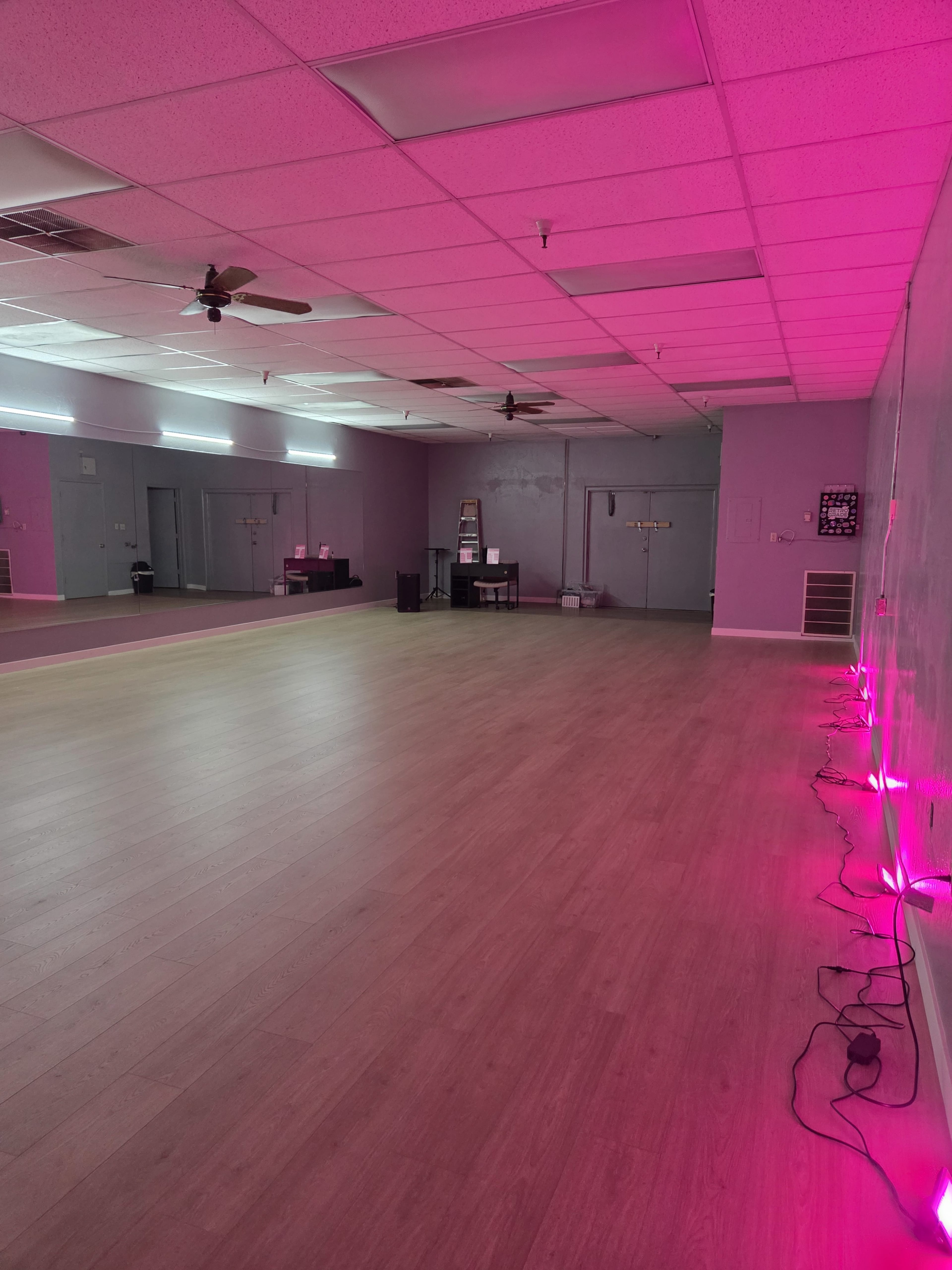 The image shows an empty studio space with wooden flooring, purple walls, and pink LED lights along the floor.