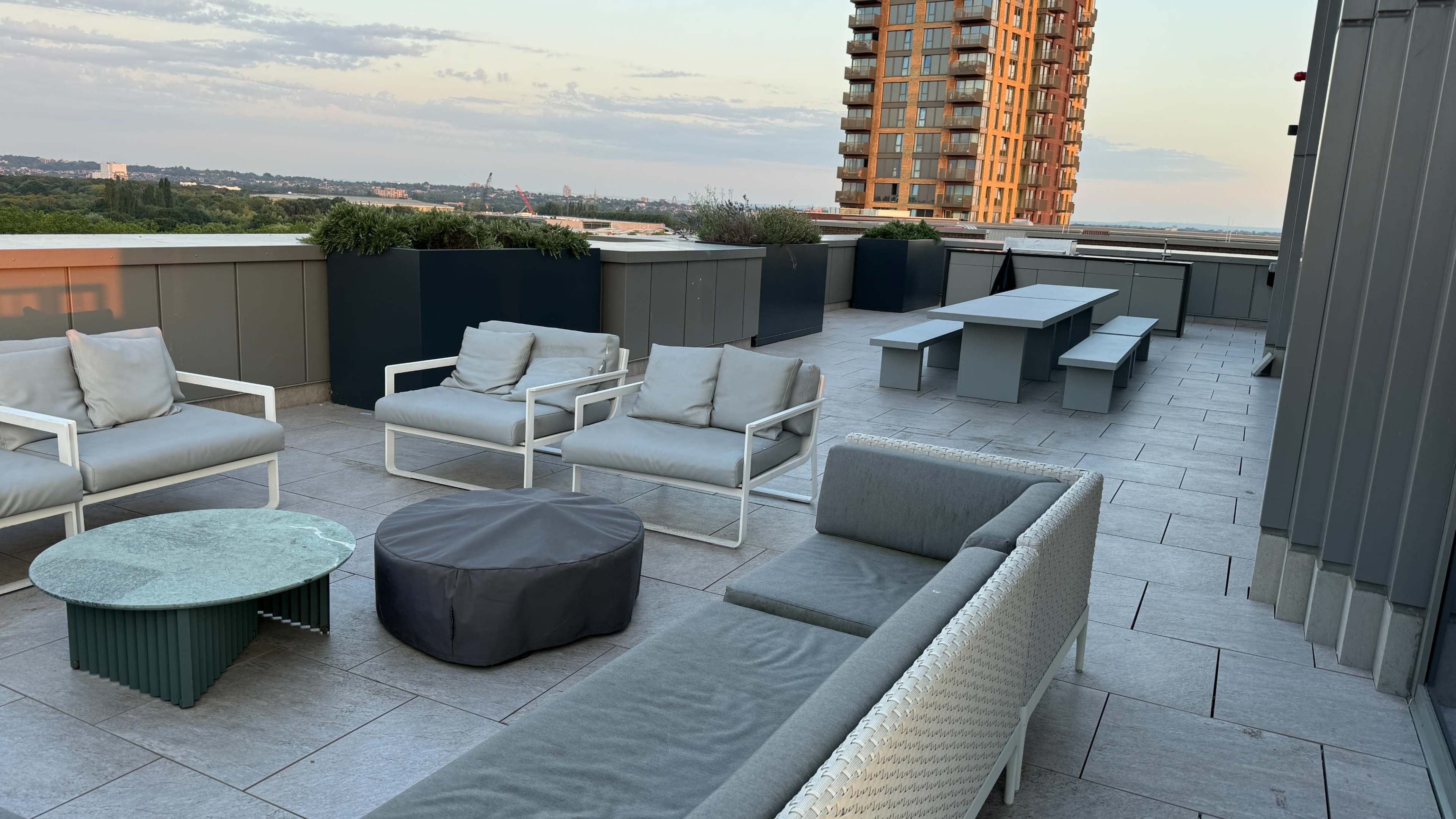 The rooftop area features a seating arrangement with several chairs, a table, and a large building in the background under a clear sky.