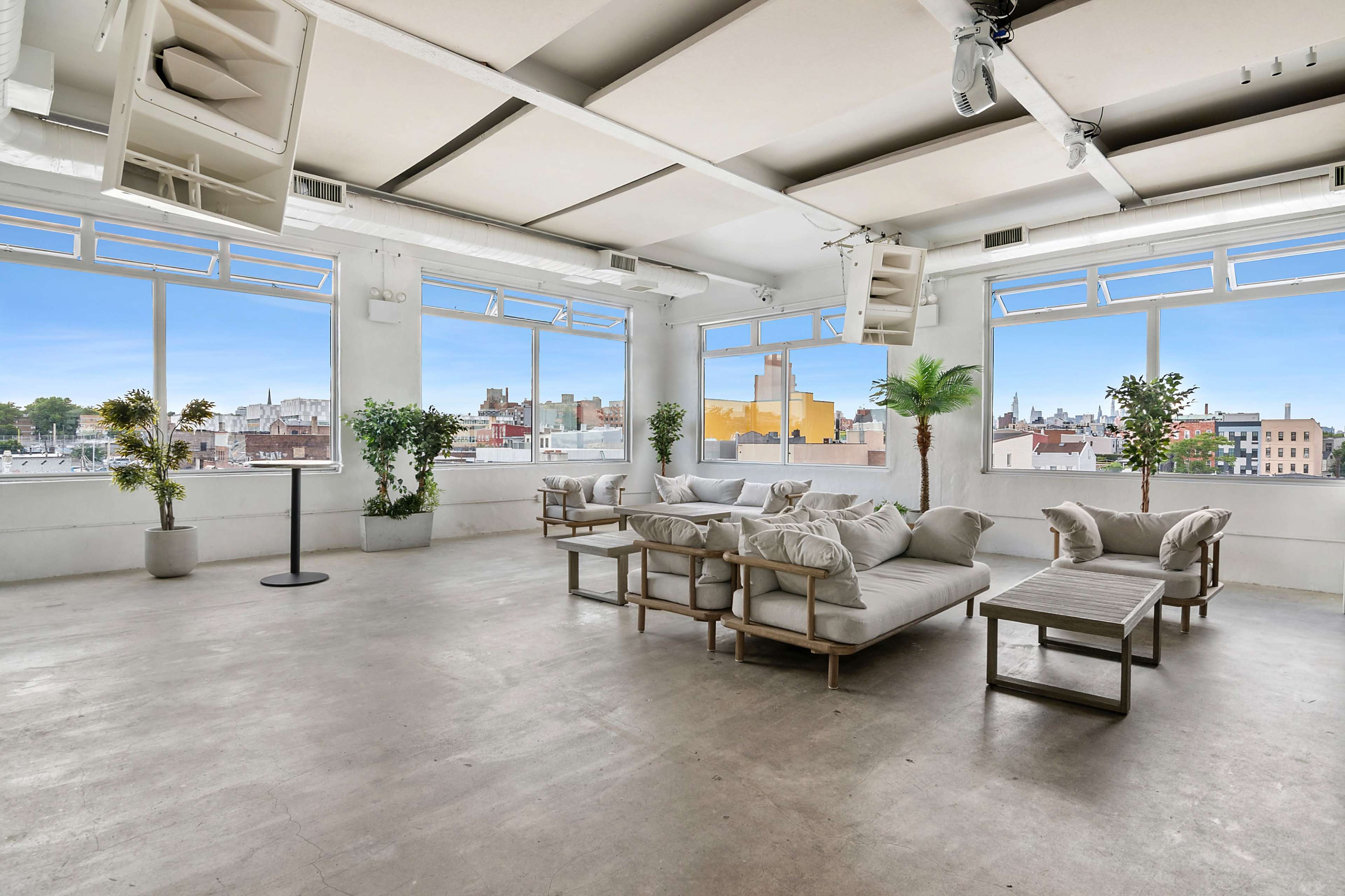 The spacious room features large windows that overlook an urban skyline, with a seating area consisting of a light-colored sofa and coffee table.