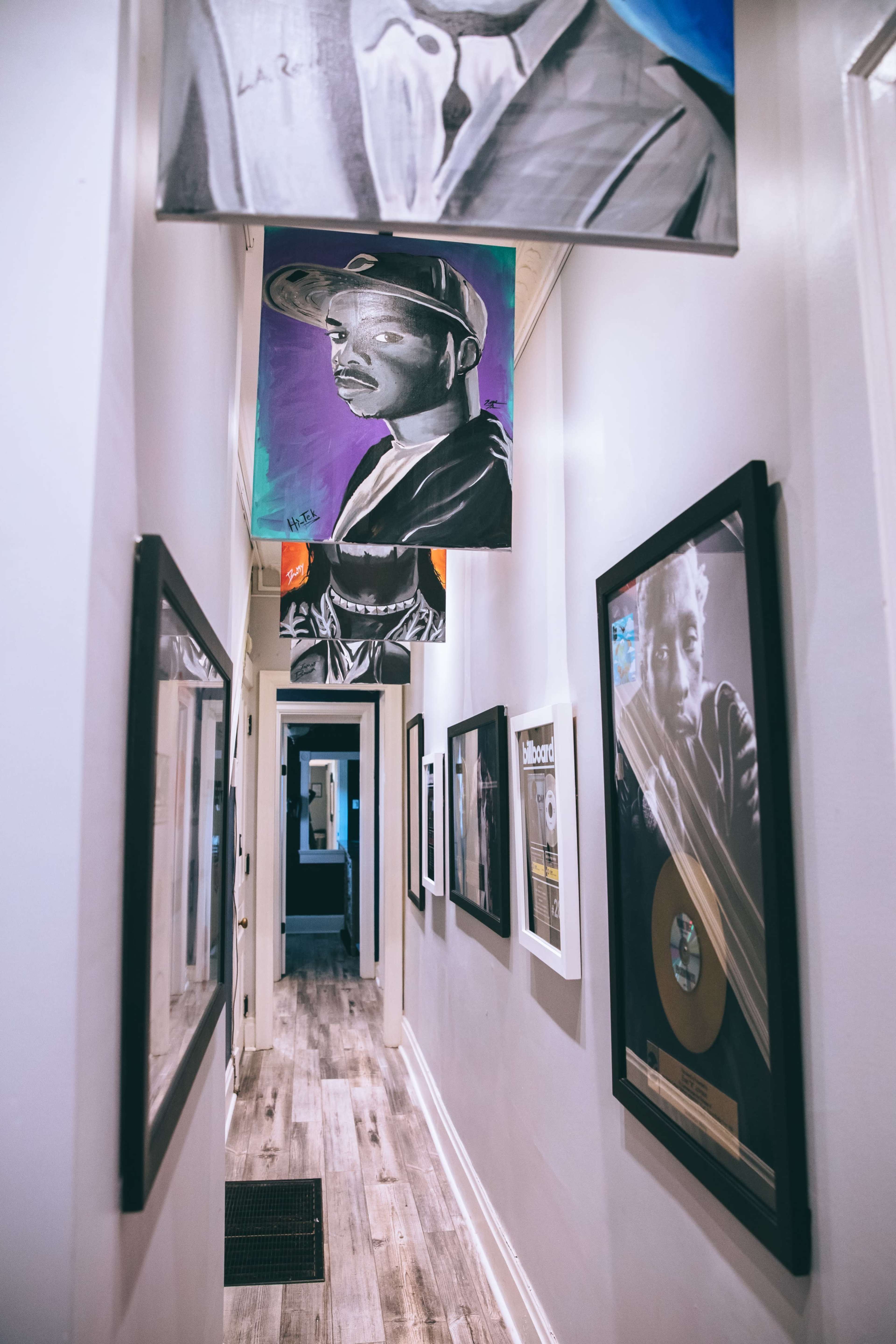 A narrow hallway lined with framed photographs and artwork, leading to an open space at the far end.