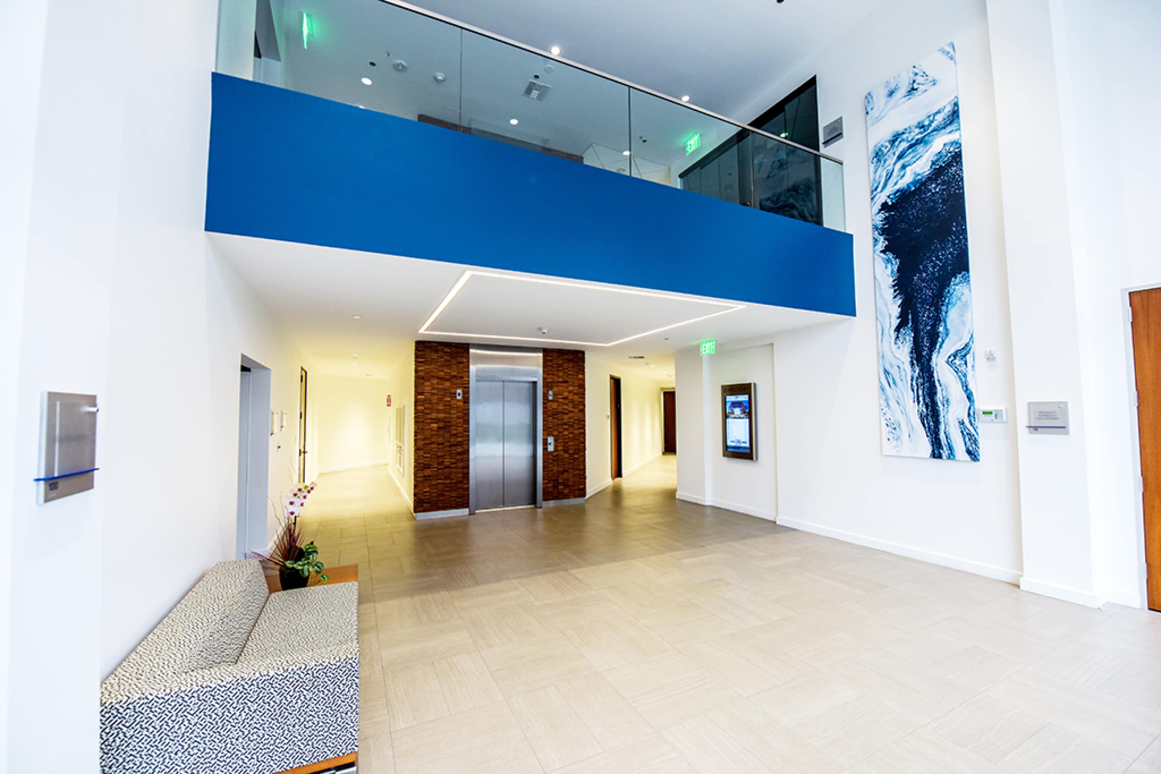 A modern interior lobby with a blue accent wall, an elevator, and a seating area featuring a patterned bench.
