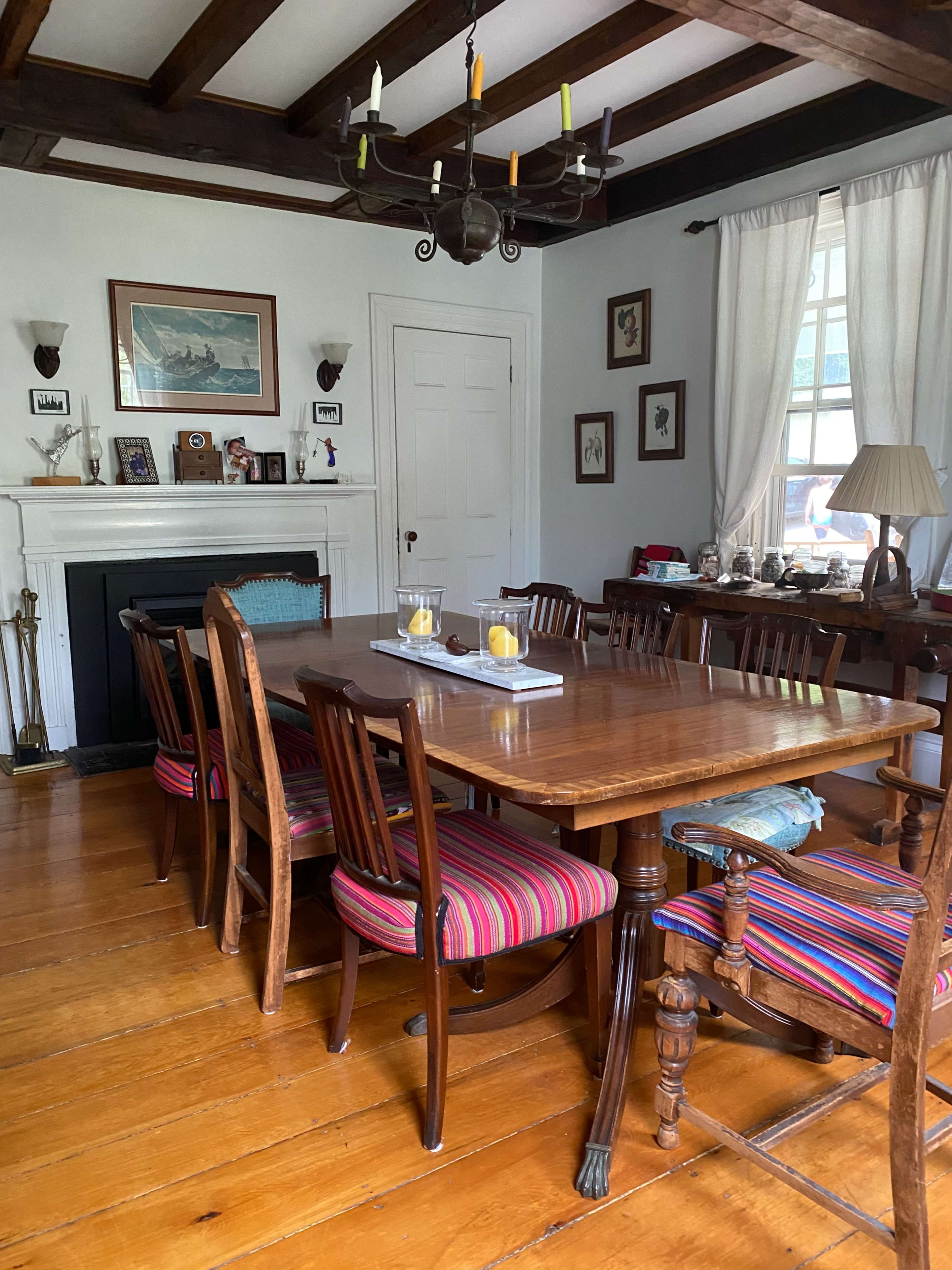 A wooden dining table surrounded by chairs with striped cushions is set in a room featuring wooden beams and a fireplace.