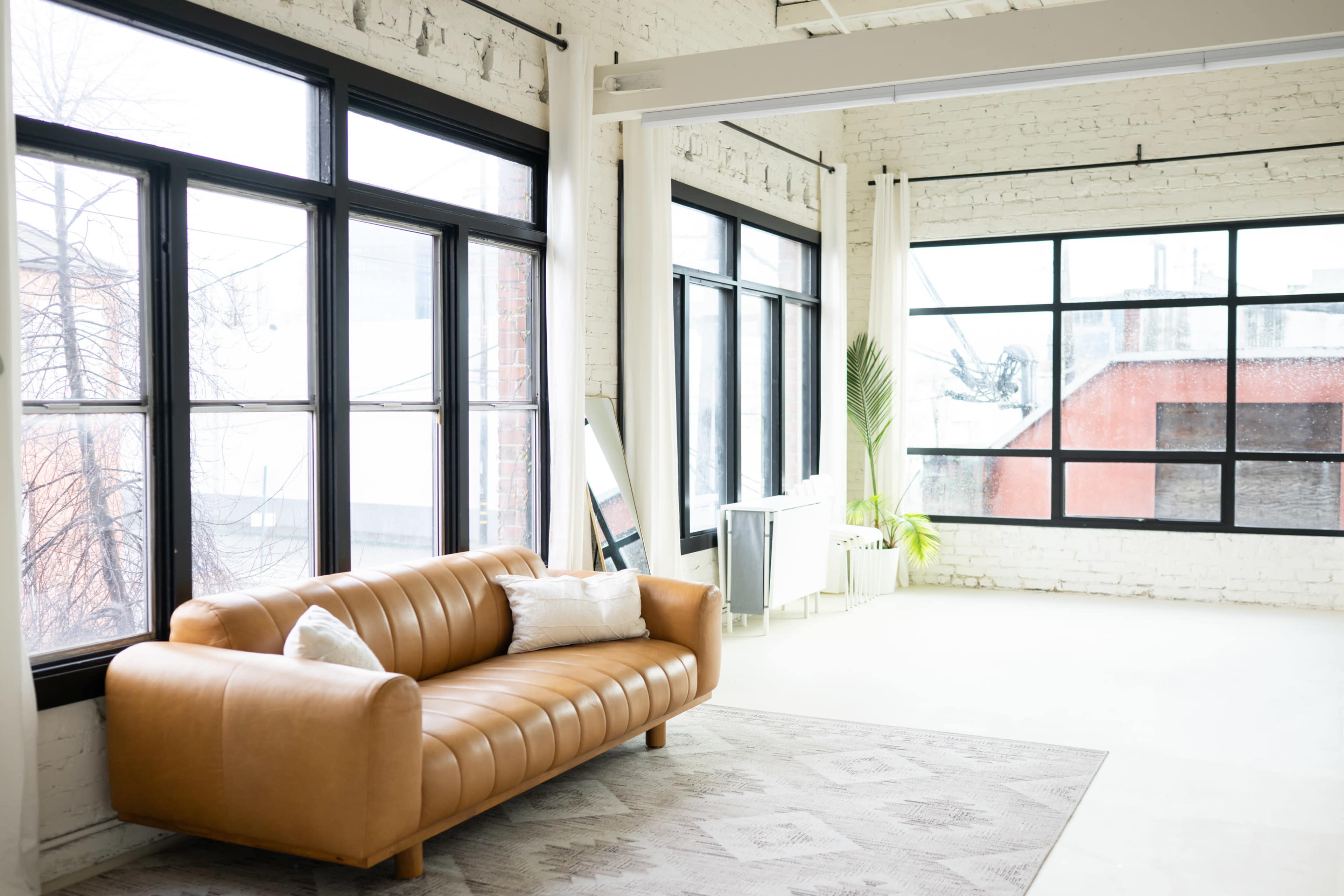 A modern living space features large windows, a brown leather couch, and minimalistic decor.