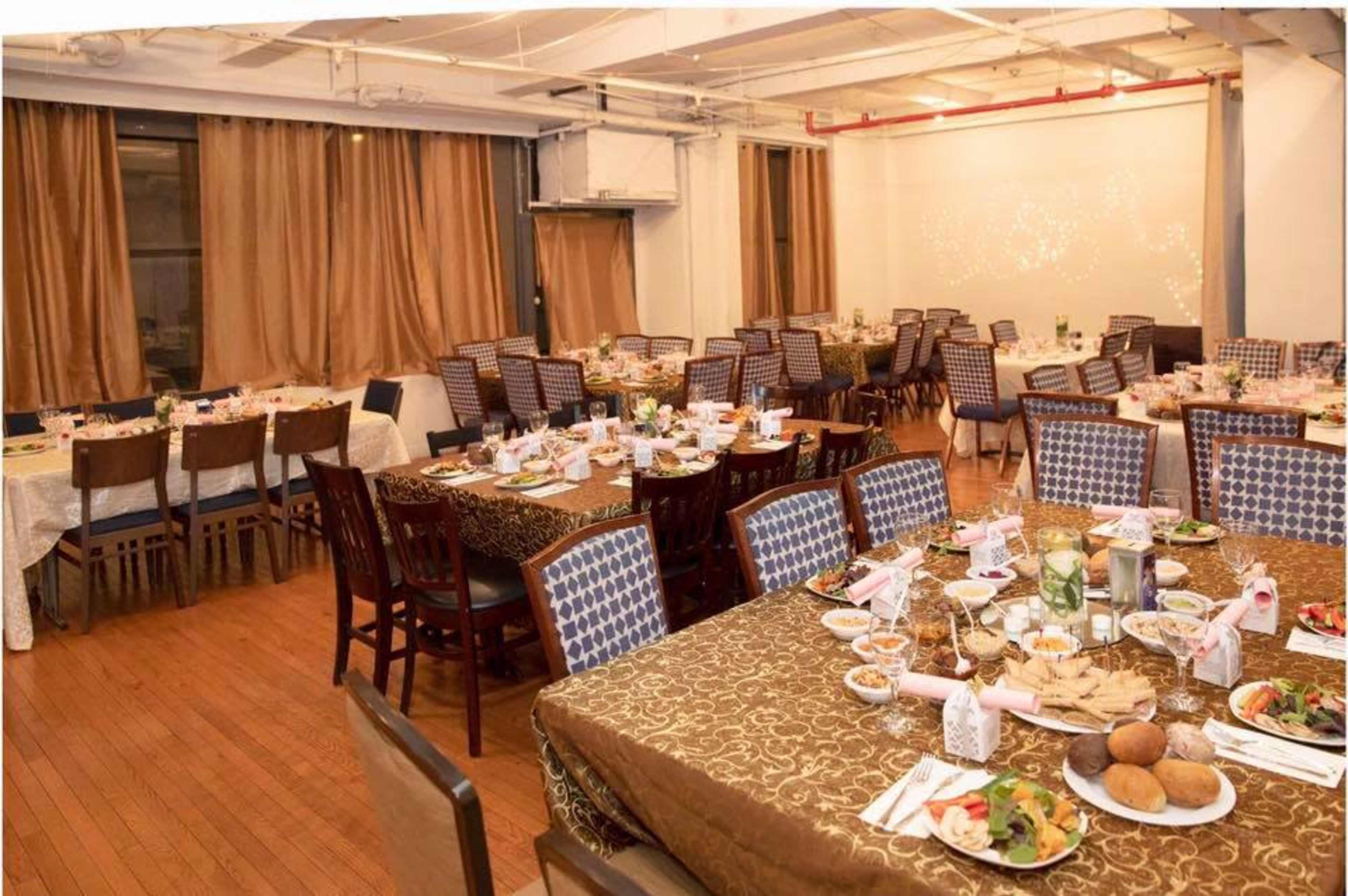 A banquet hall with multiple tables set for a formal dinner, featuring tablecloths, place settings, and a variety of food.