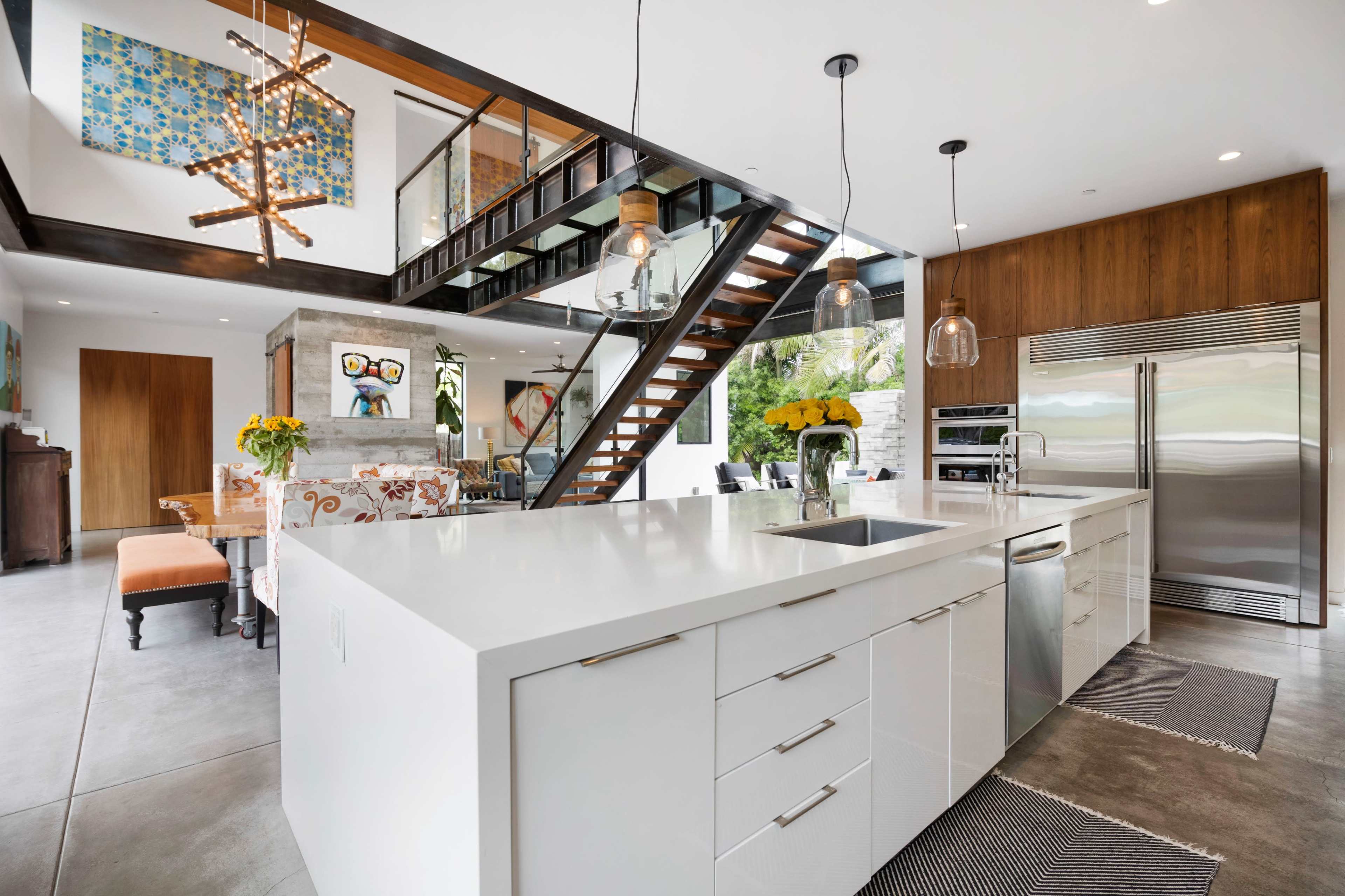 A modern kitchen with a large white island, stainless steel appliances, and an open staircase leading to an upper level.