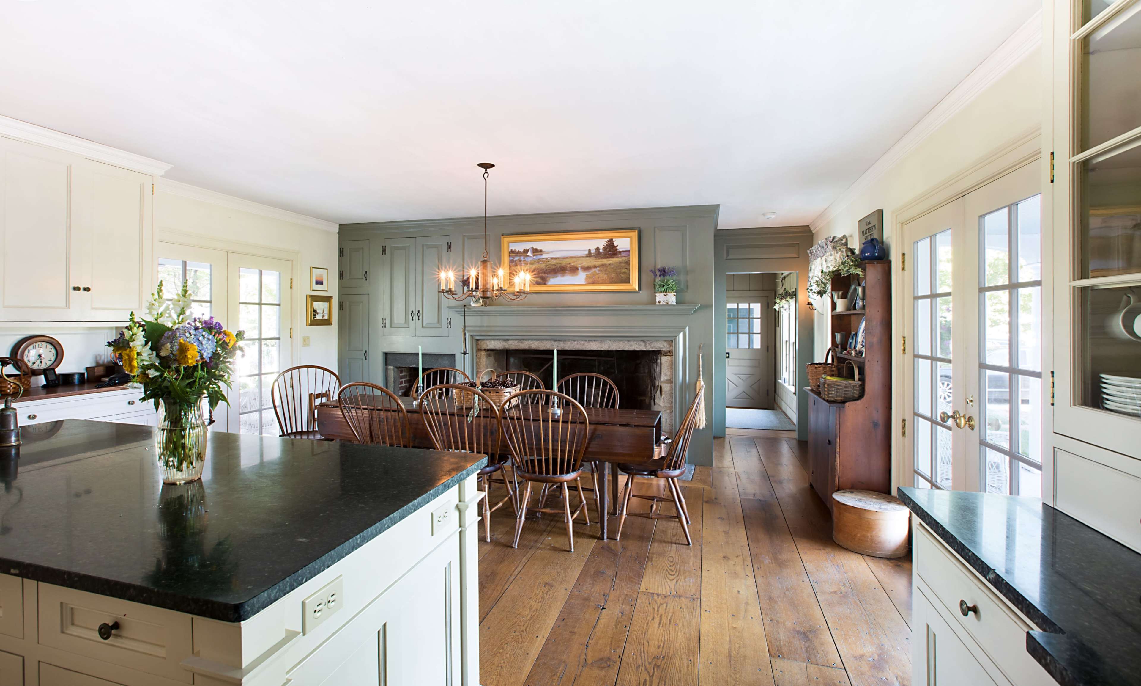 A spacious kitchen with a large wooden dining table surrounded by chairs, featuring a stone fireplace and a bouquet of flowers on the countertop.