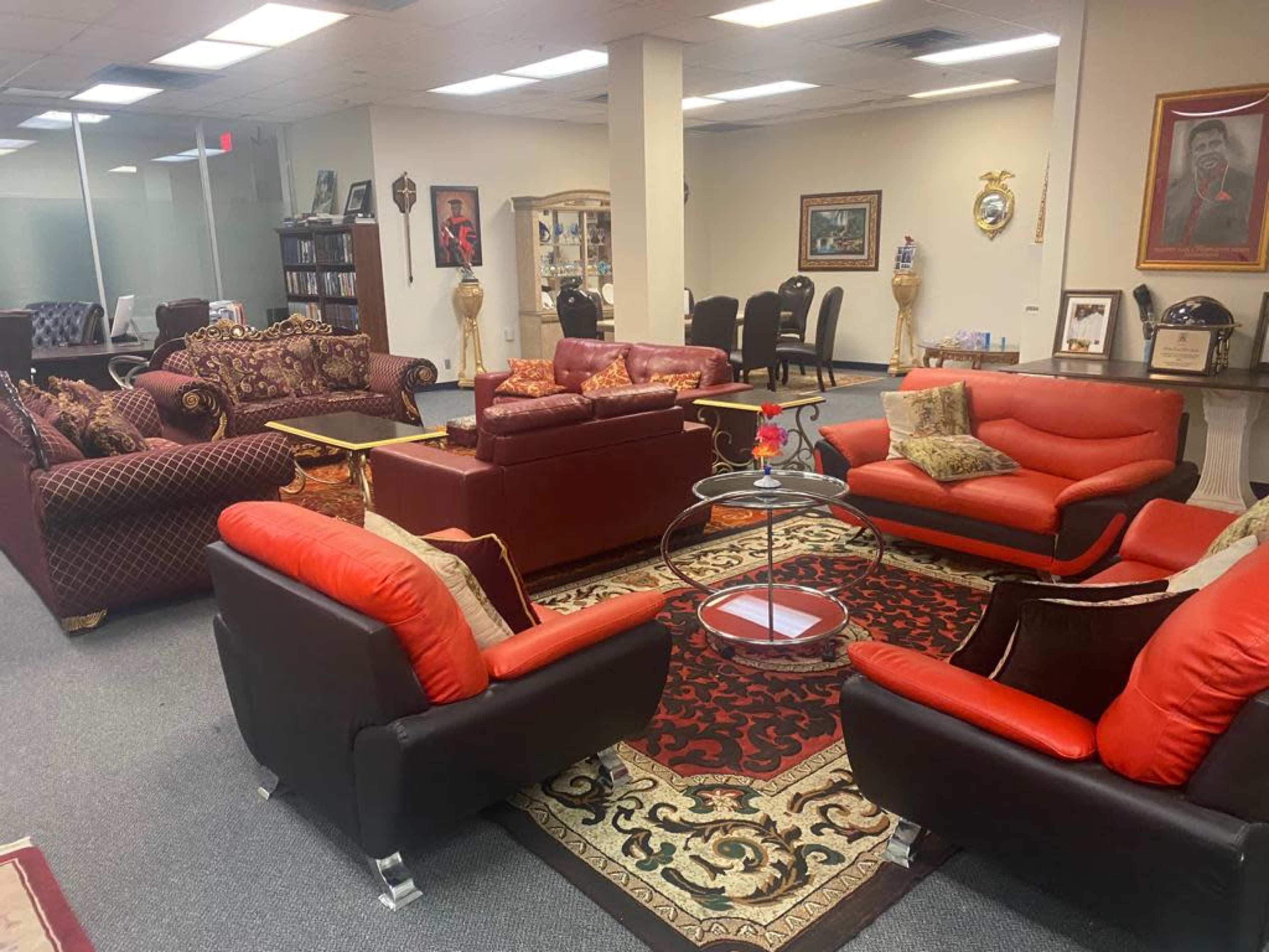 A furnished office lounge area with several seating arrangements, including red and black couches, a glass coffee table, and decorative rugs on the floor.
