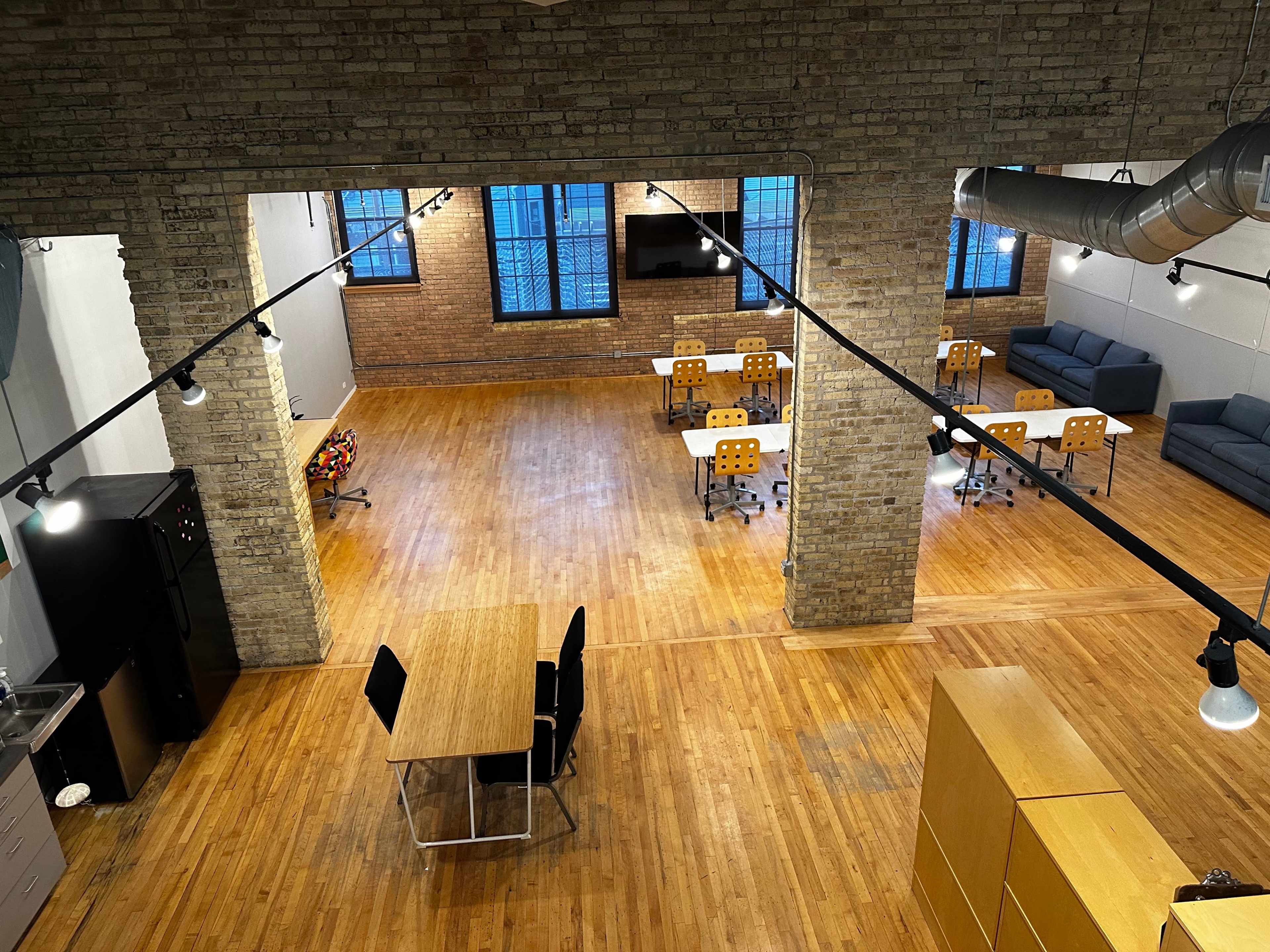 A spacious office interior with wooden floors, exposed brick walls, and several workstations arranged around a central meeting table.
