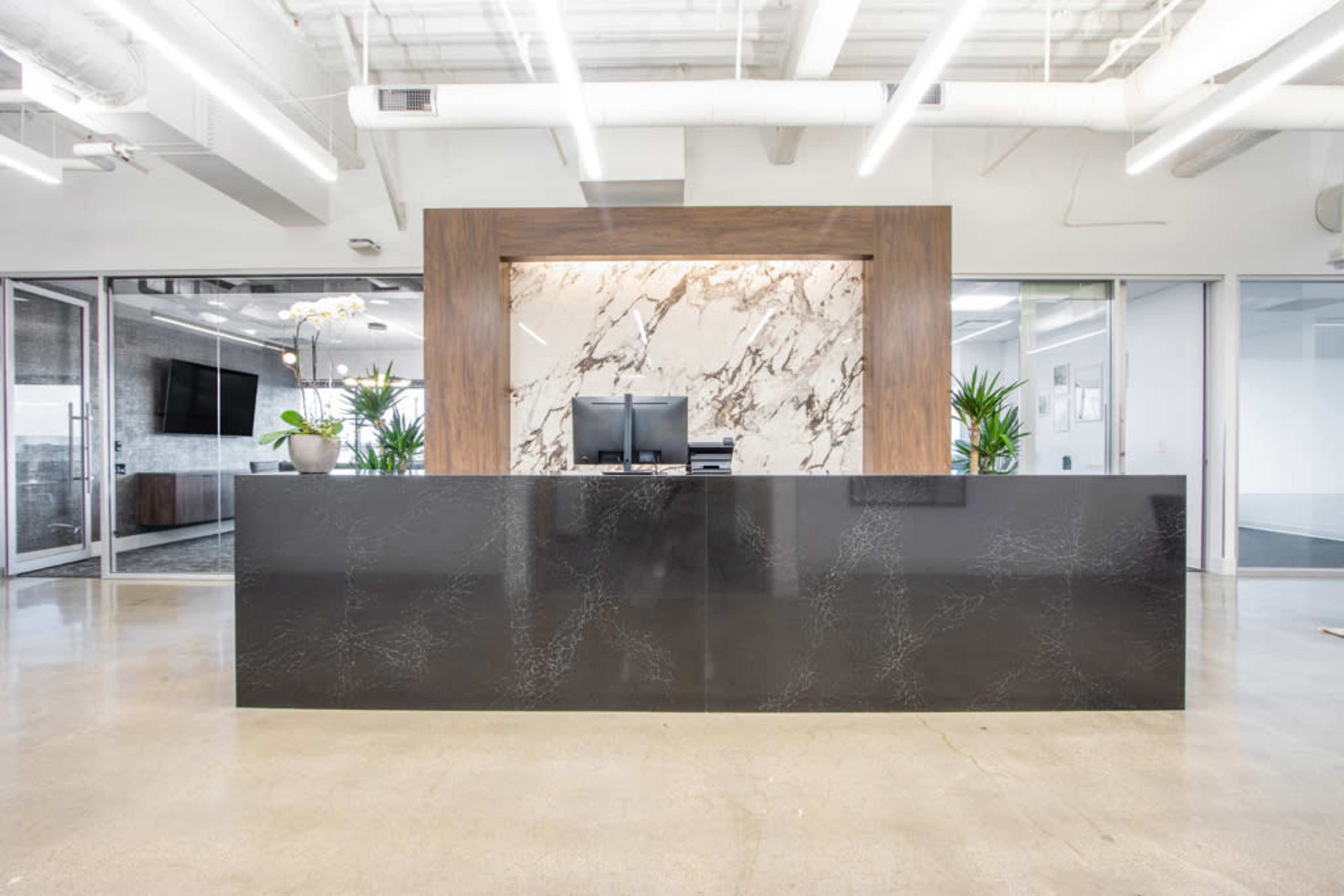 A modern reception area features a sleek, dark countertop with a marble backdrop and two computer monitors.