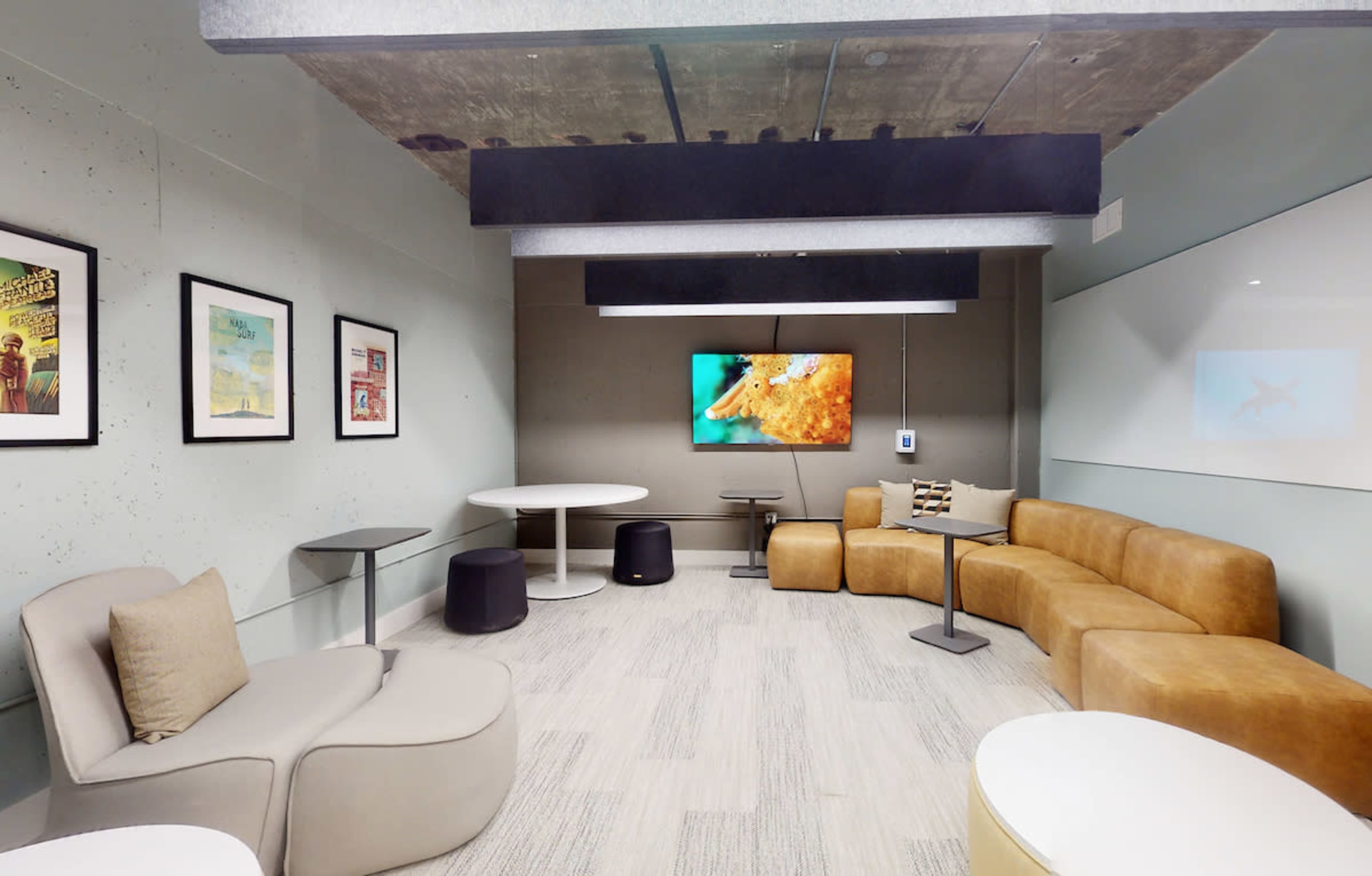 A modern lounge room features a curved brown couch, two tables, and framed artwork on the walls, with a television displaying an underwater image.