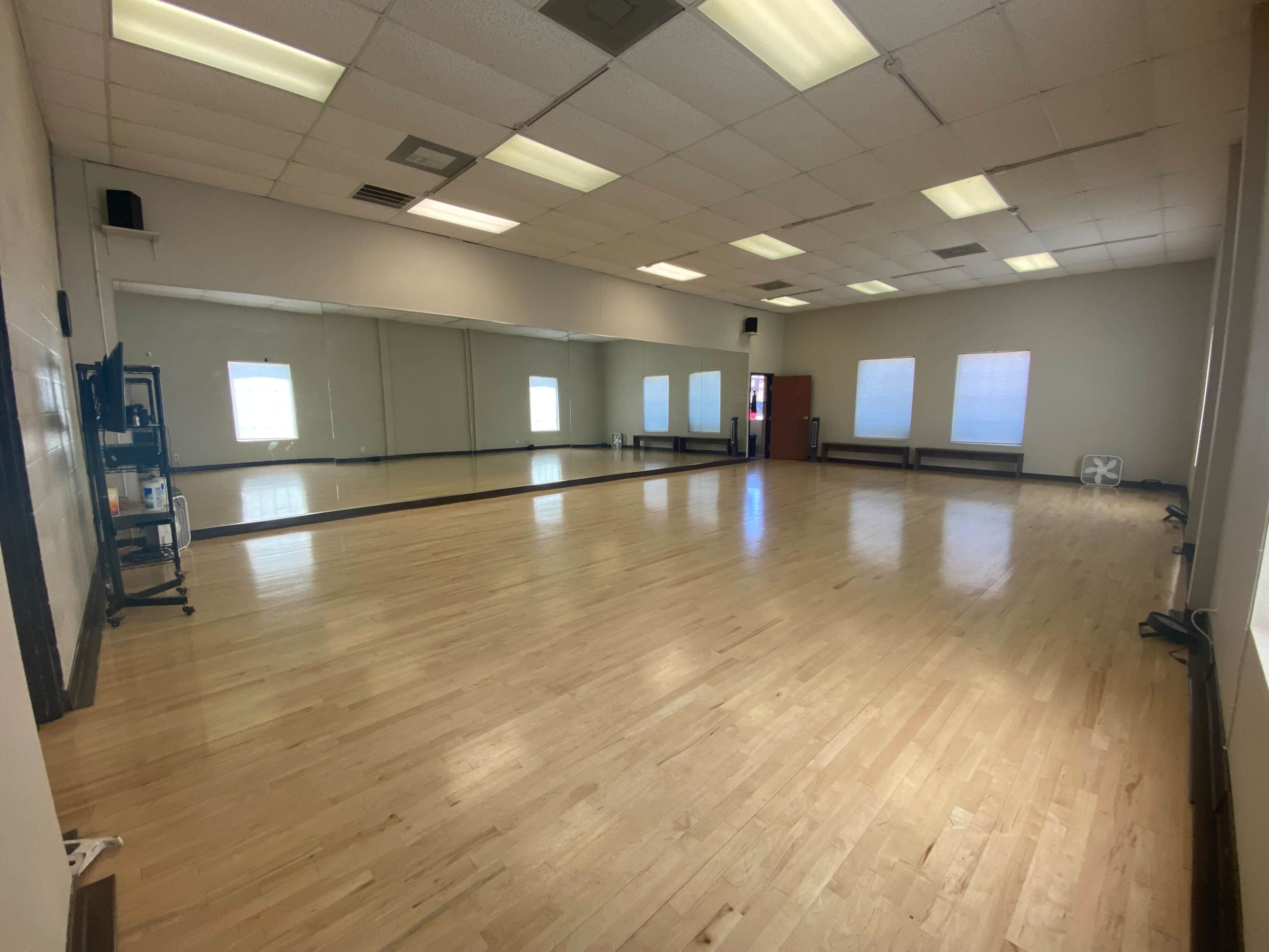 A spacious, empty dance studio with wooden flooring and large mirrors on one wall.