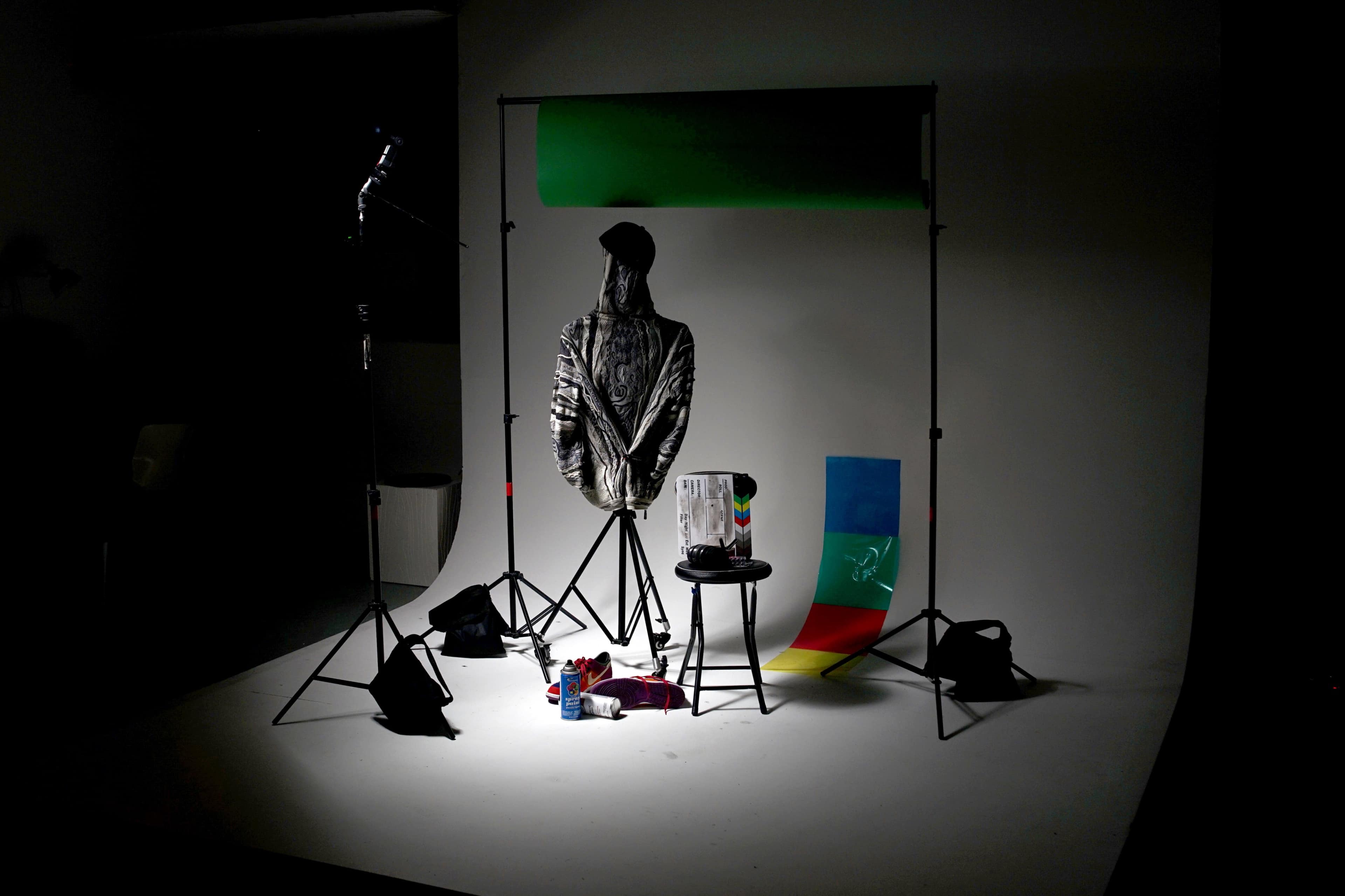 The image depicts a photography studio setup featuring a mannequin dressed in a reflective garment, a chair, various colored backdrops, and scattered props on the floor.