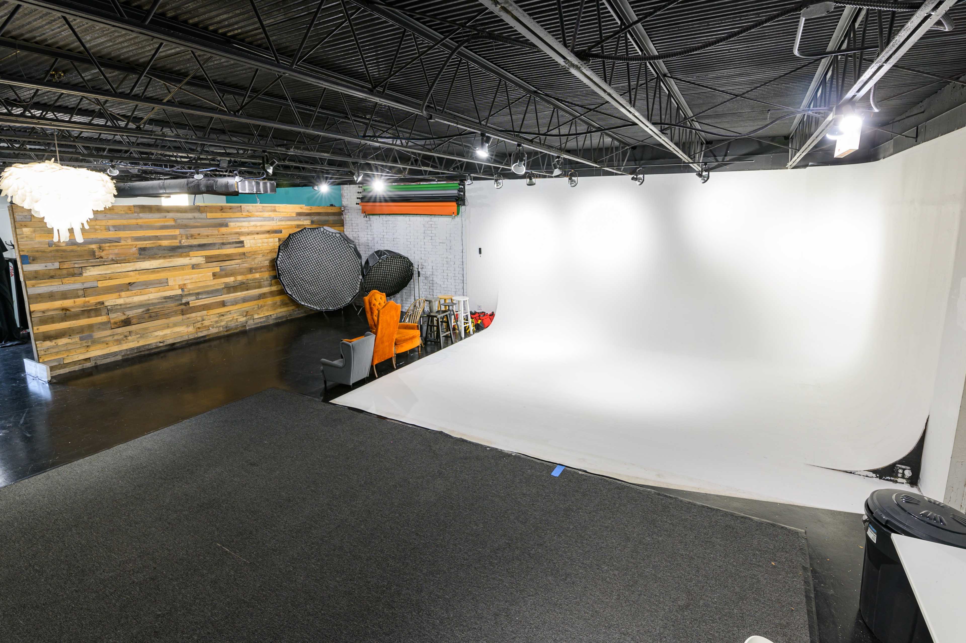 A photography studio with a seamless white backdrop, wooden accent wall, and various lighting equipment.