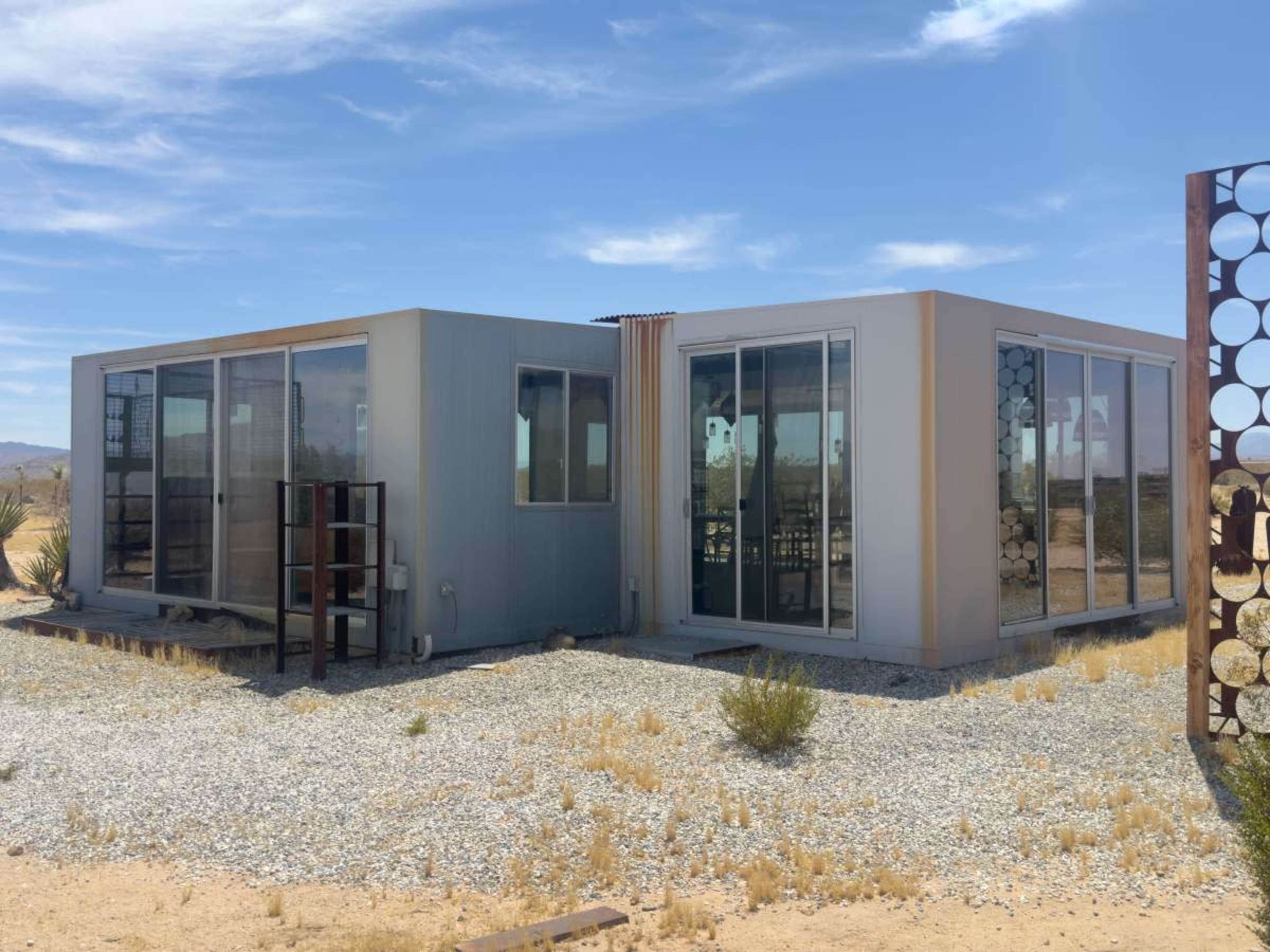 The image shows a modern, modular building with large glass windows set in a desert landscape.
