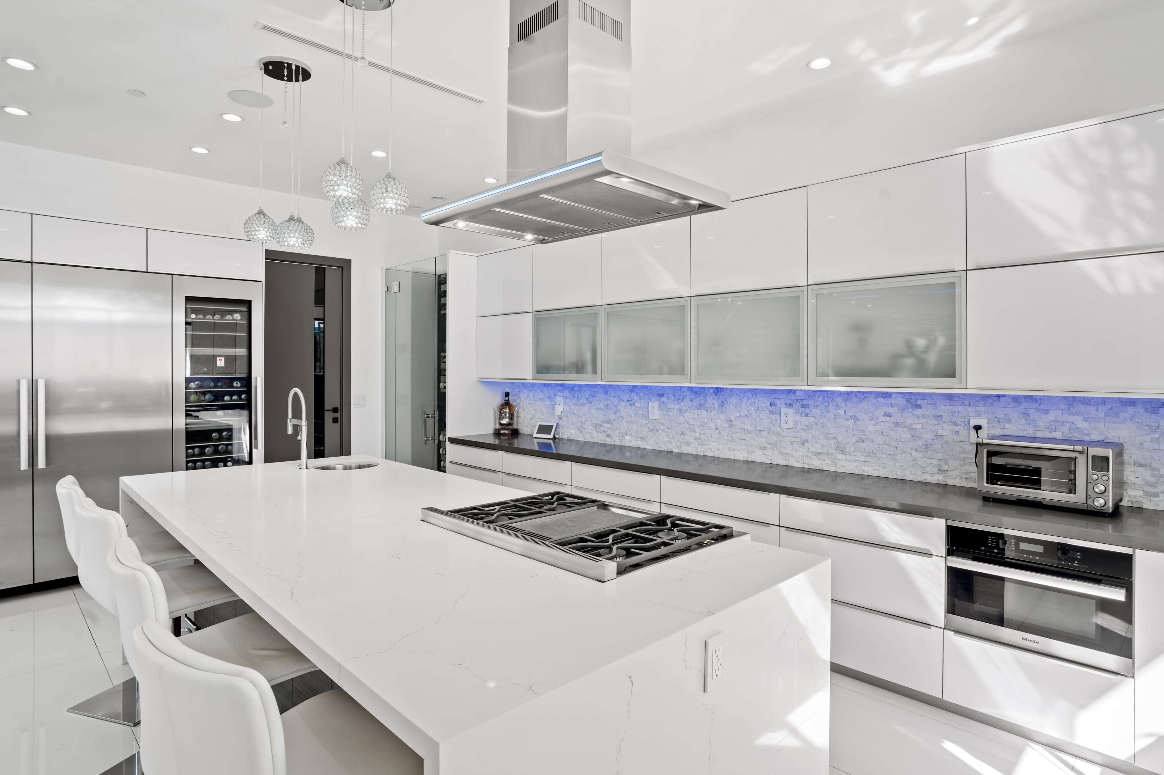 The modern kitchen features sleek white cabinetry, a spacious island with a gas cooktop, and under-cabinet lighting along the backsplash.