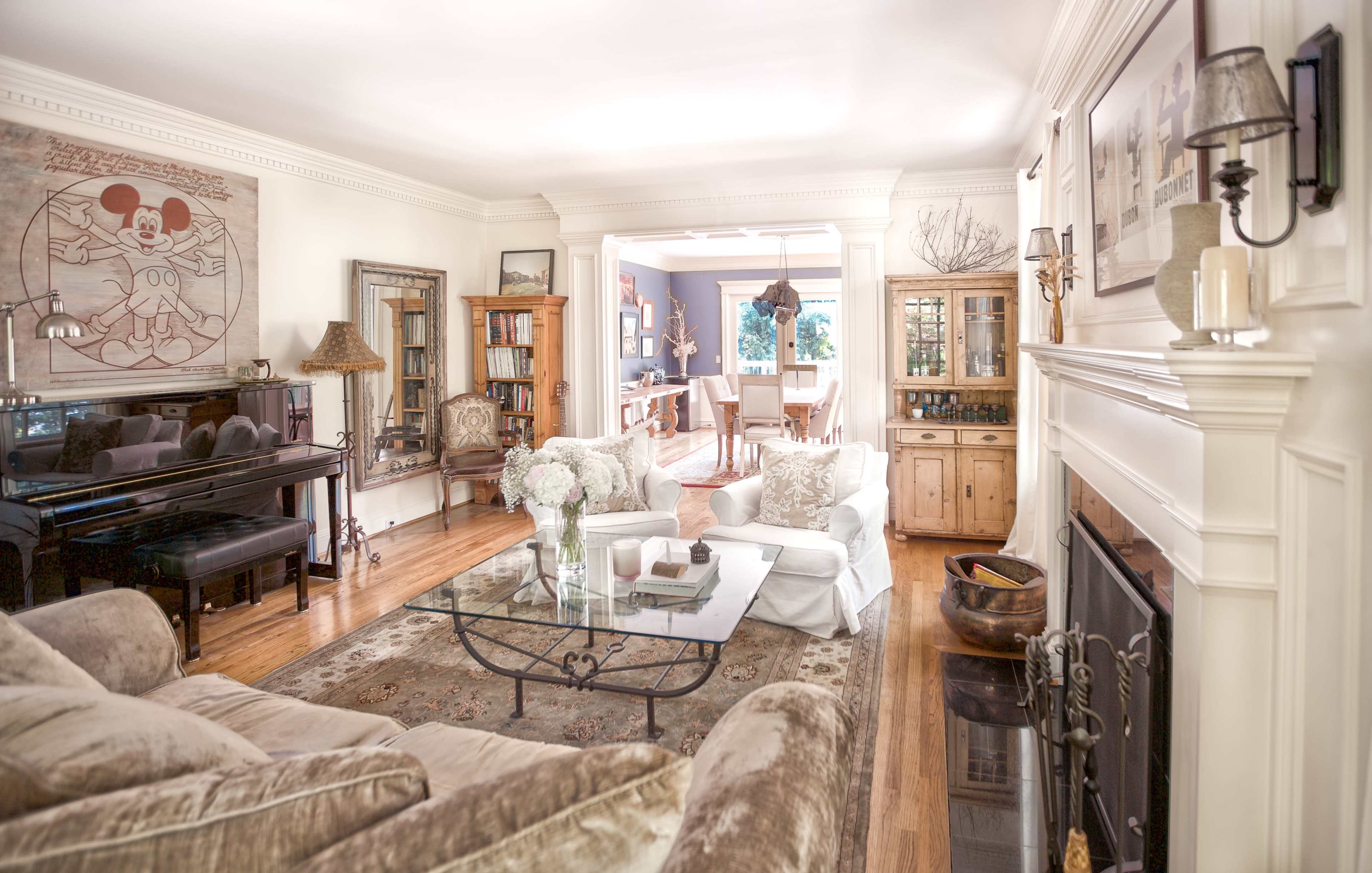 A well-lit living room with a piano, a glass coffee table, beige sofas, and a view of the dining area through an open space.