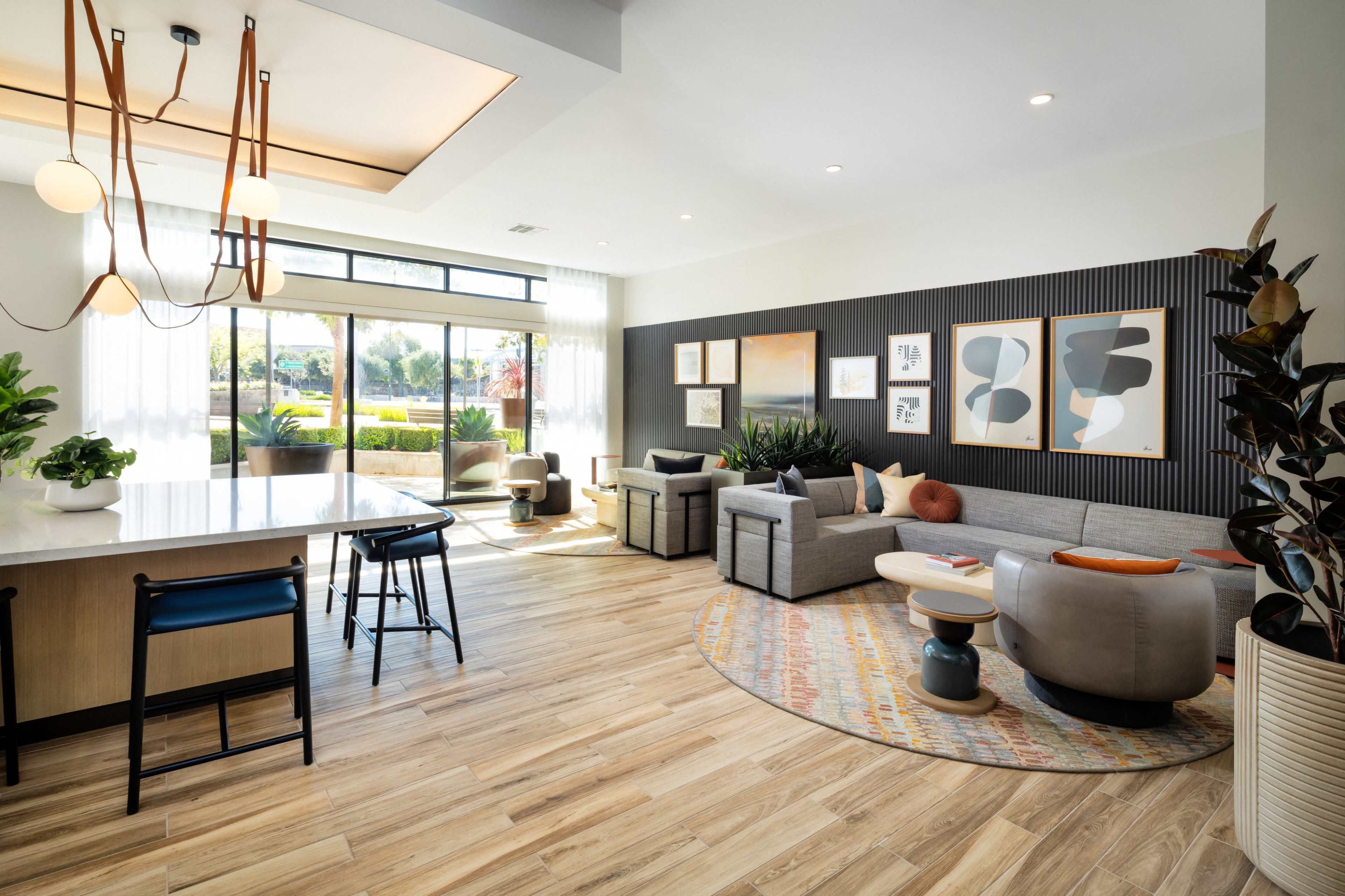 The image shows a modern living area with a gray sectional sofa, a round coffee table, and large windows allowing natural light to fill the space.