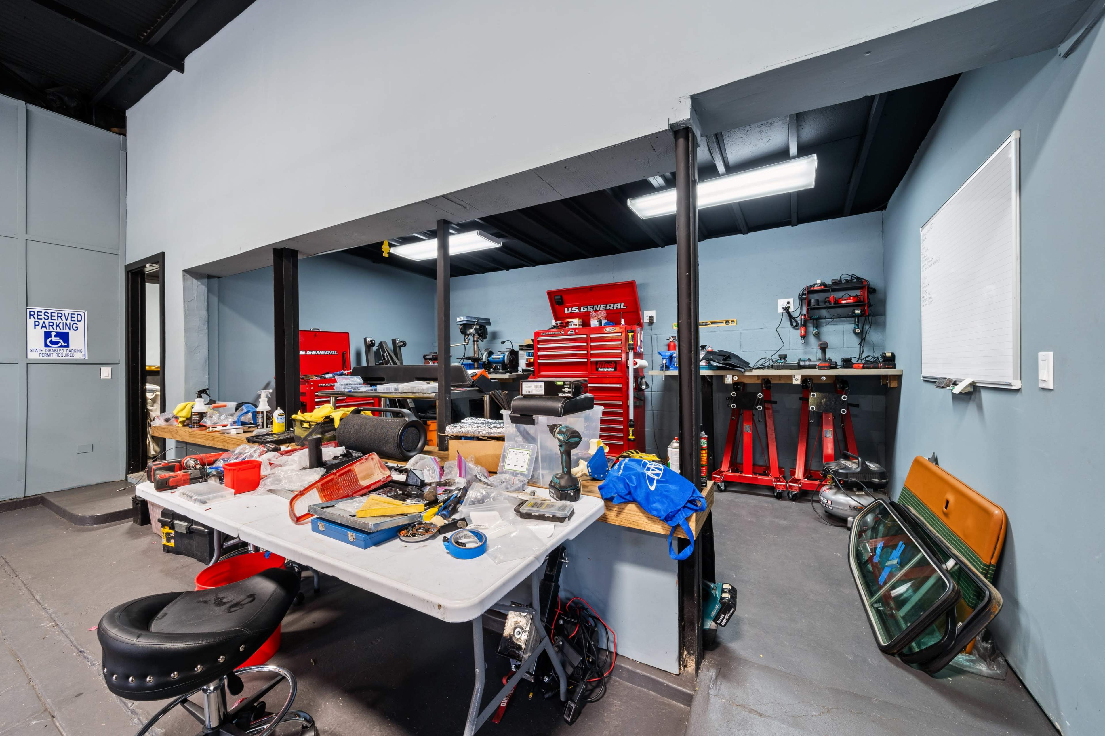 The image shows a garage workshop with a cluttered table in the foreground and tool storage at the back, including a red tool chest and various workbench equipment.