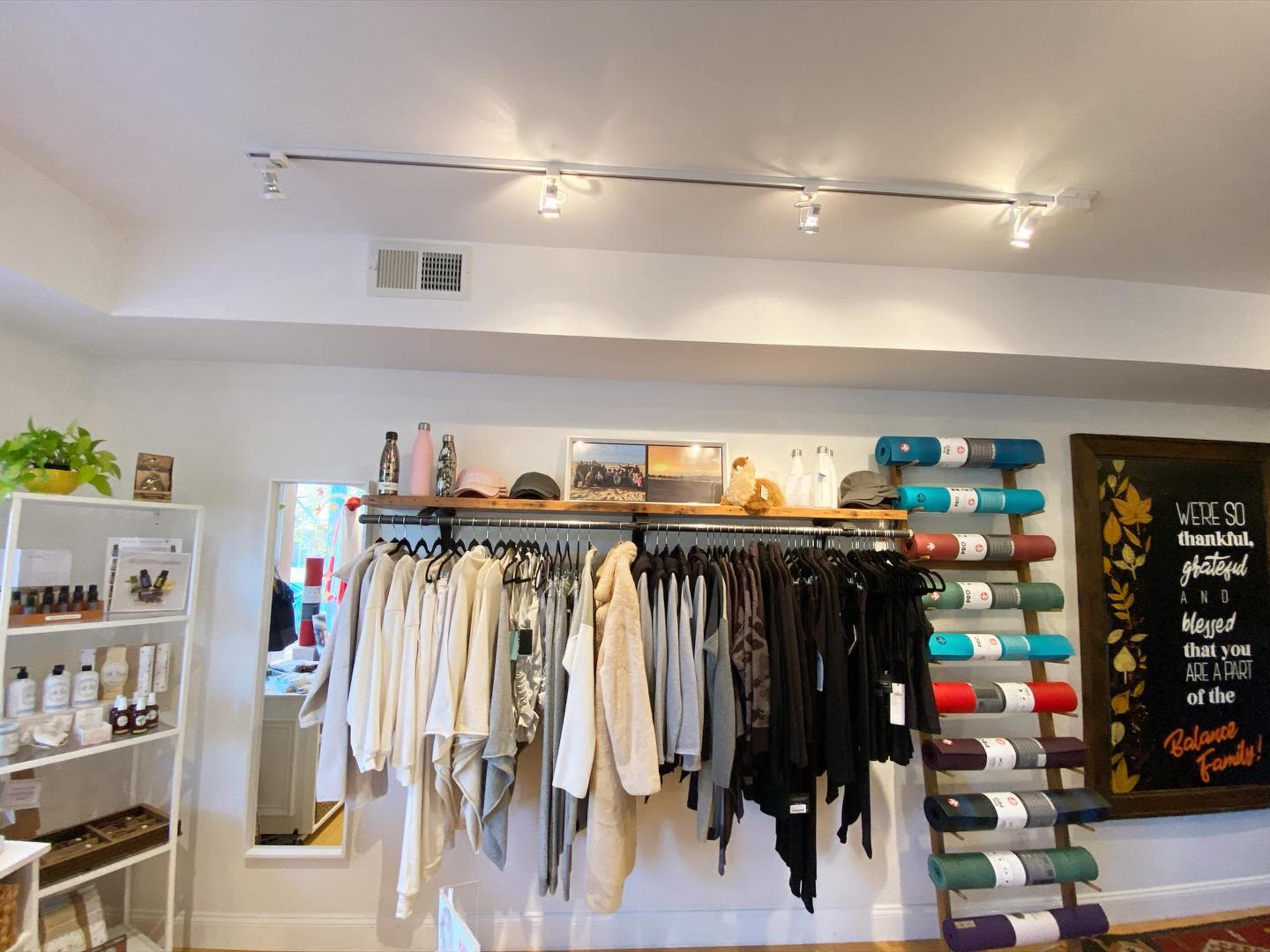 A clothing and wellness shop featuring a display of apparel hanging on a rack and yoga mats arranged on the wall.