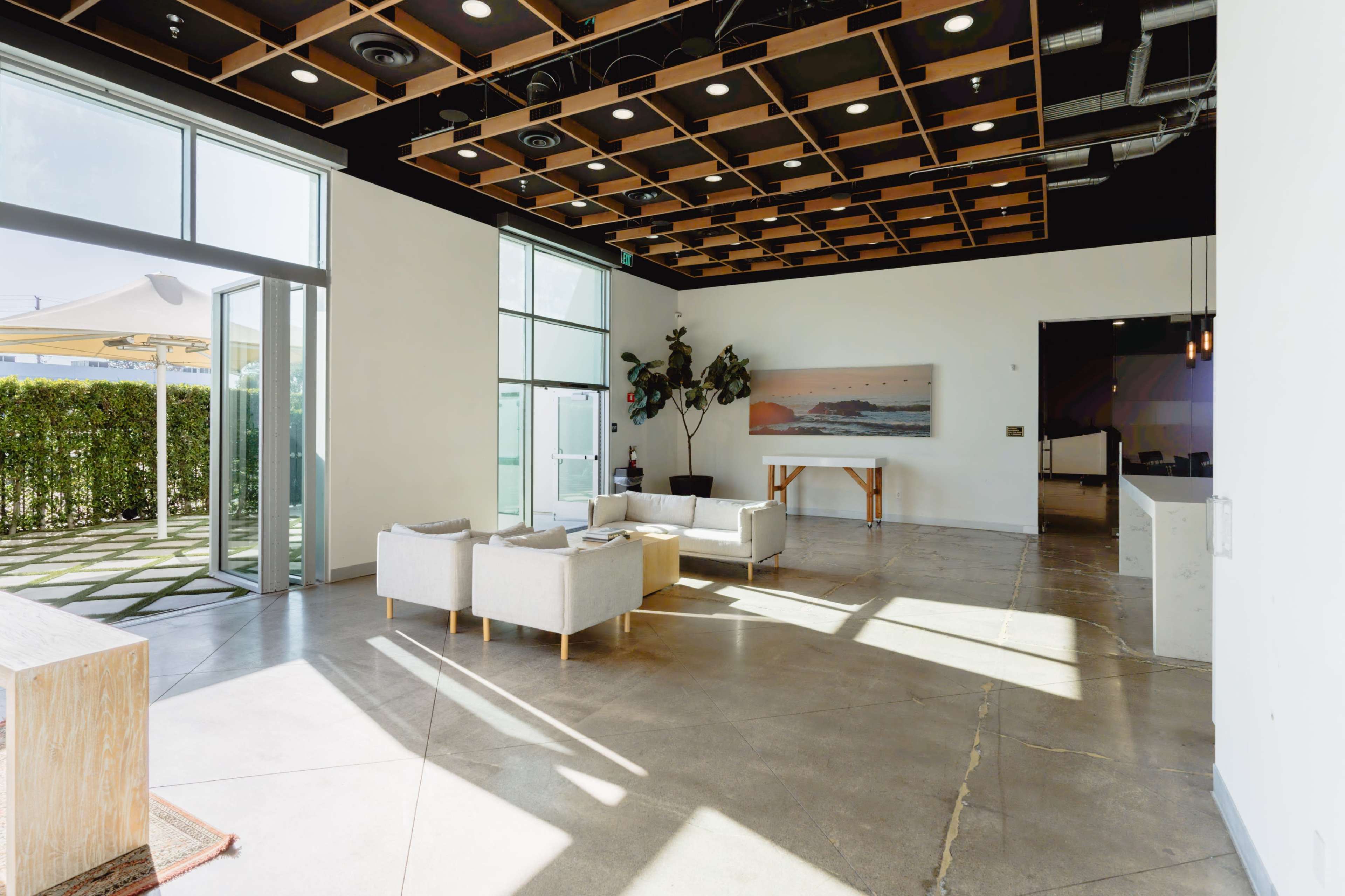 The image shows a modern, open interior space featuring a seating area with light-colored furniture and large windows that let in natural light.