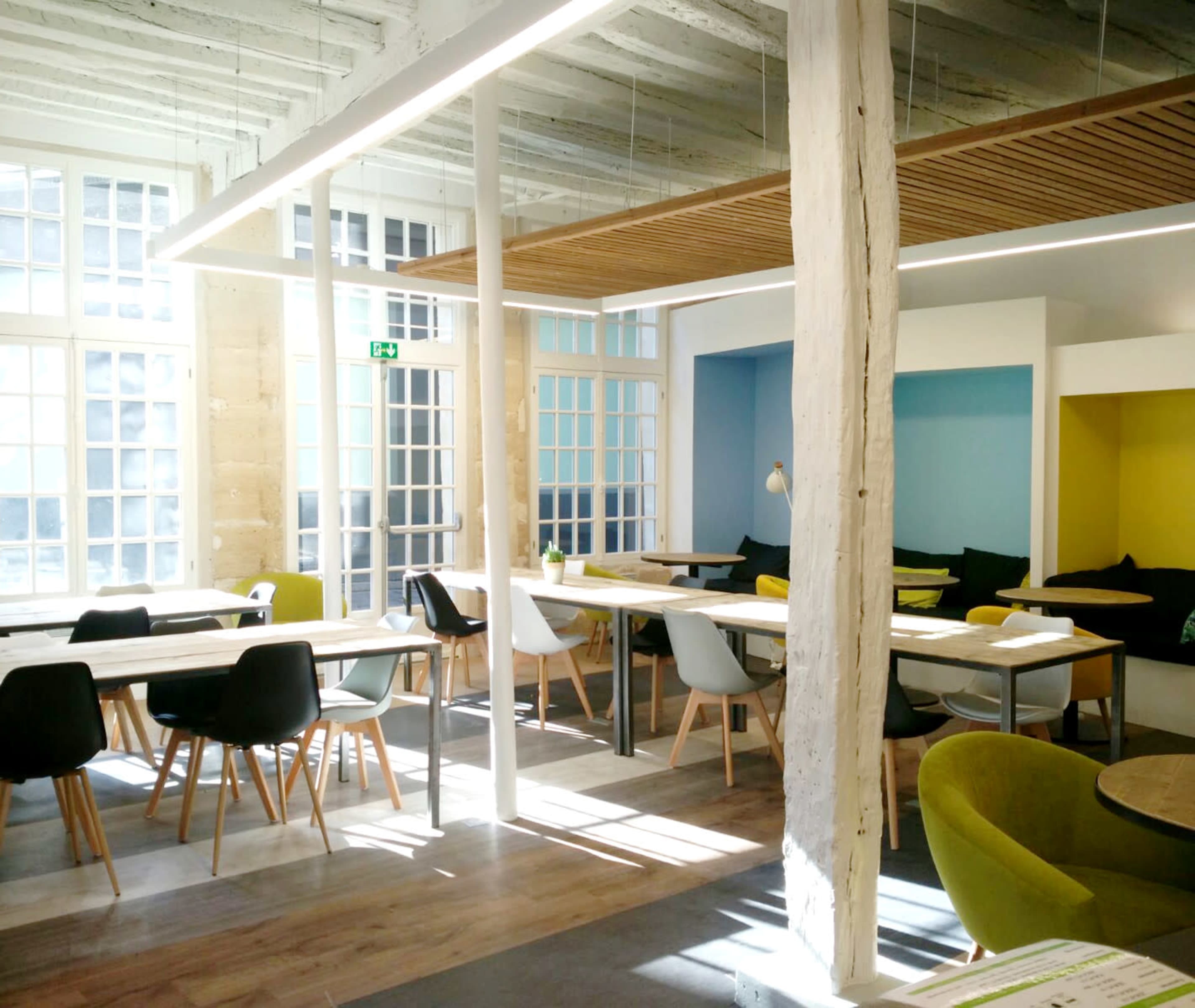 A modern, airy café with various seating arrangements, large windows, and colorful accent walls.