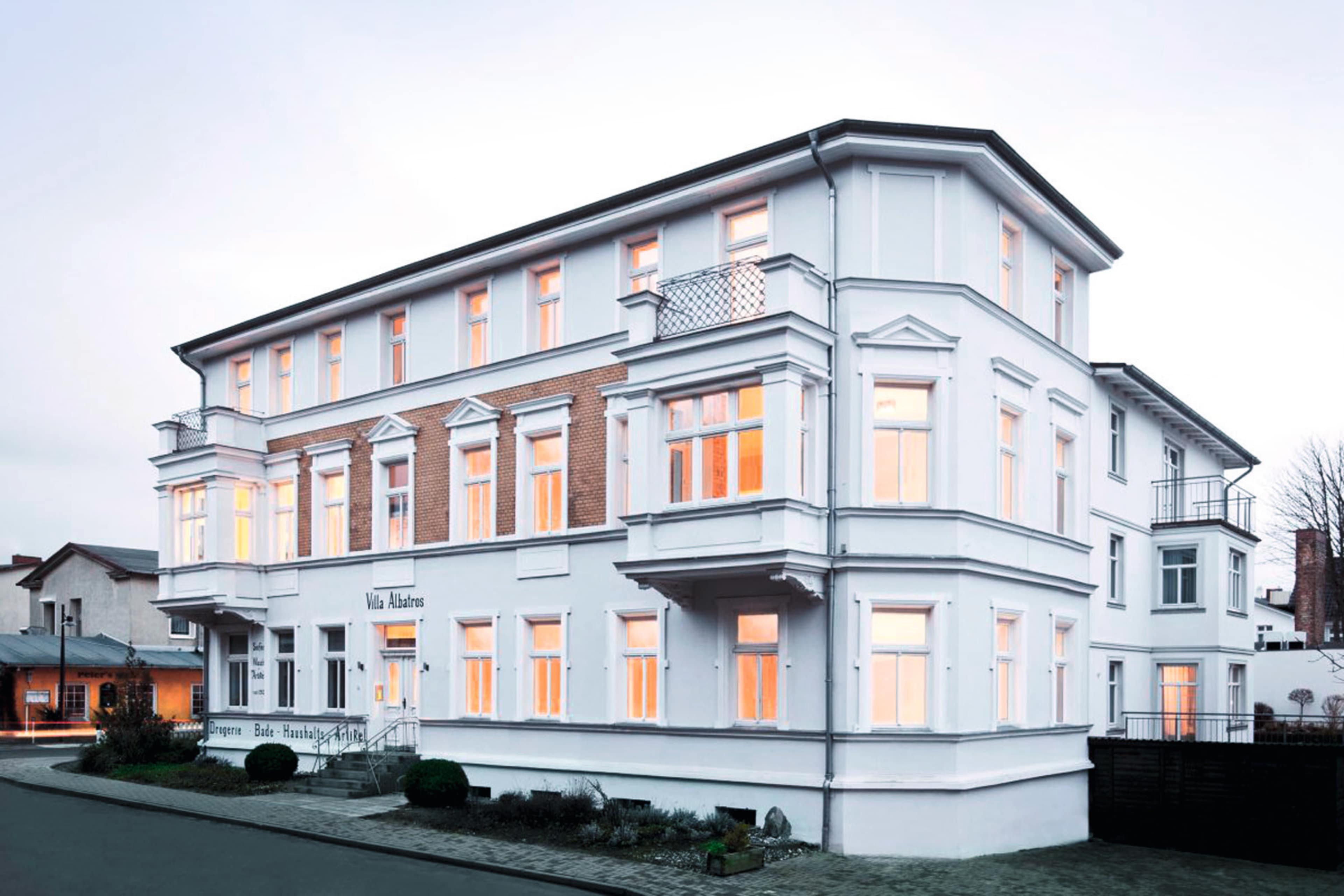 A three-story white building with numerous windows is located on a street, featuring a classic architectural design.