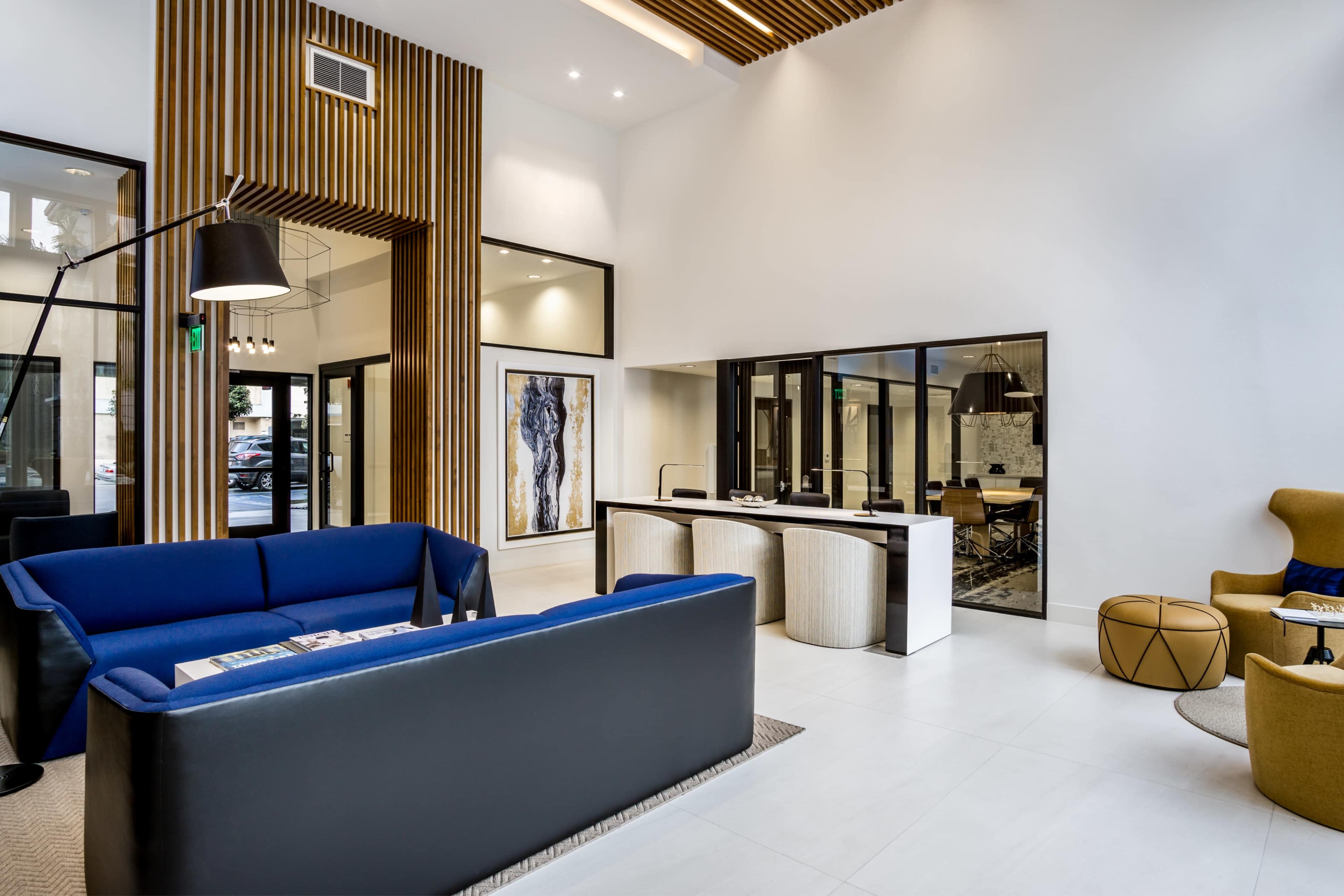 A modern lobby with a blue couch, wooden accents on the walls, and a reception area featuring light-colored furniture.