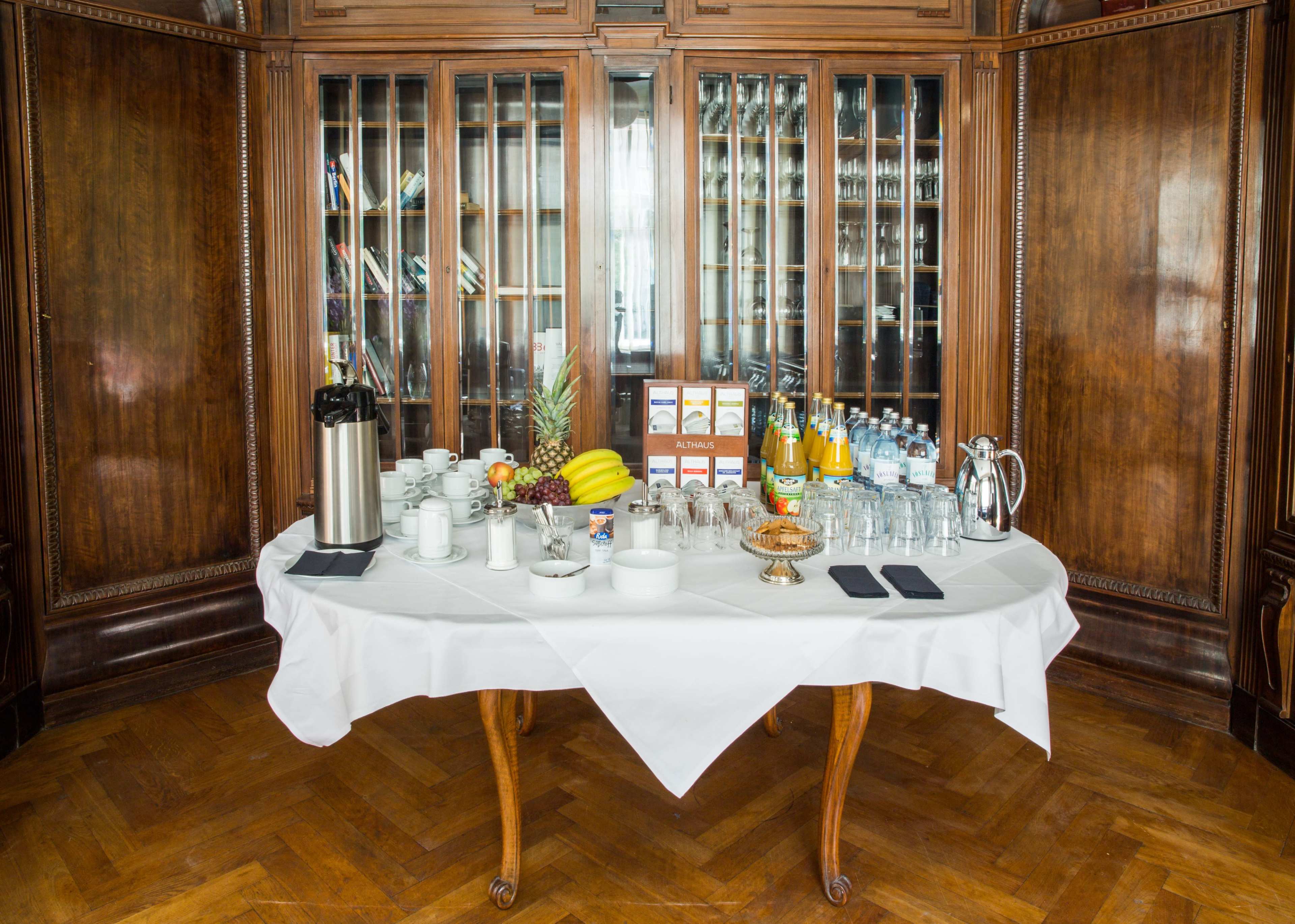 A table is set up with beverages, glassware, fruits, and snacks in a wooden-paneled room.