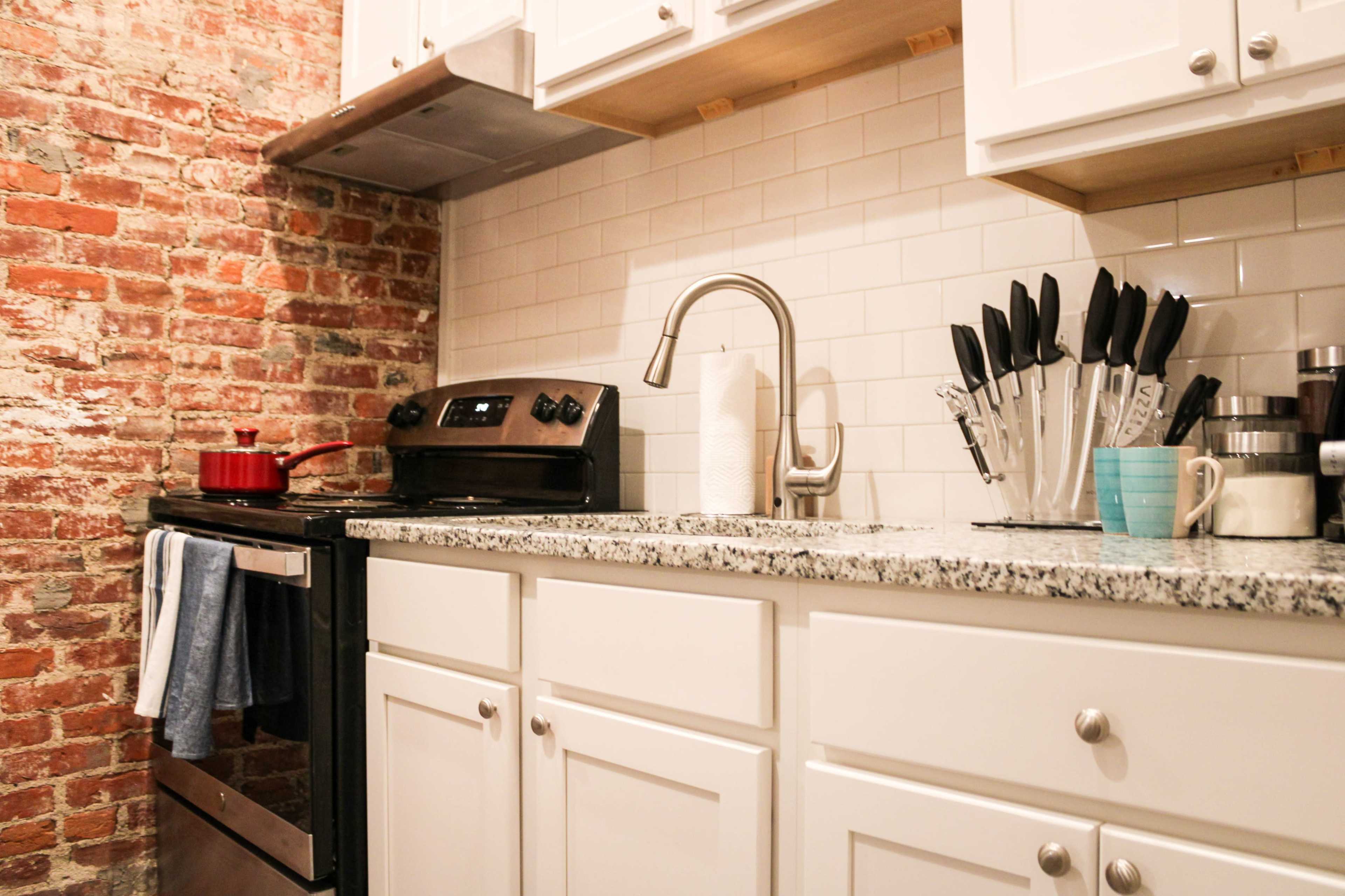 A kitchen featuring exposed brick walls, a stainless steel stove, and a countertop with various kitchen utensils arranged in a holder.