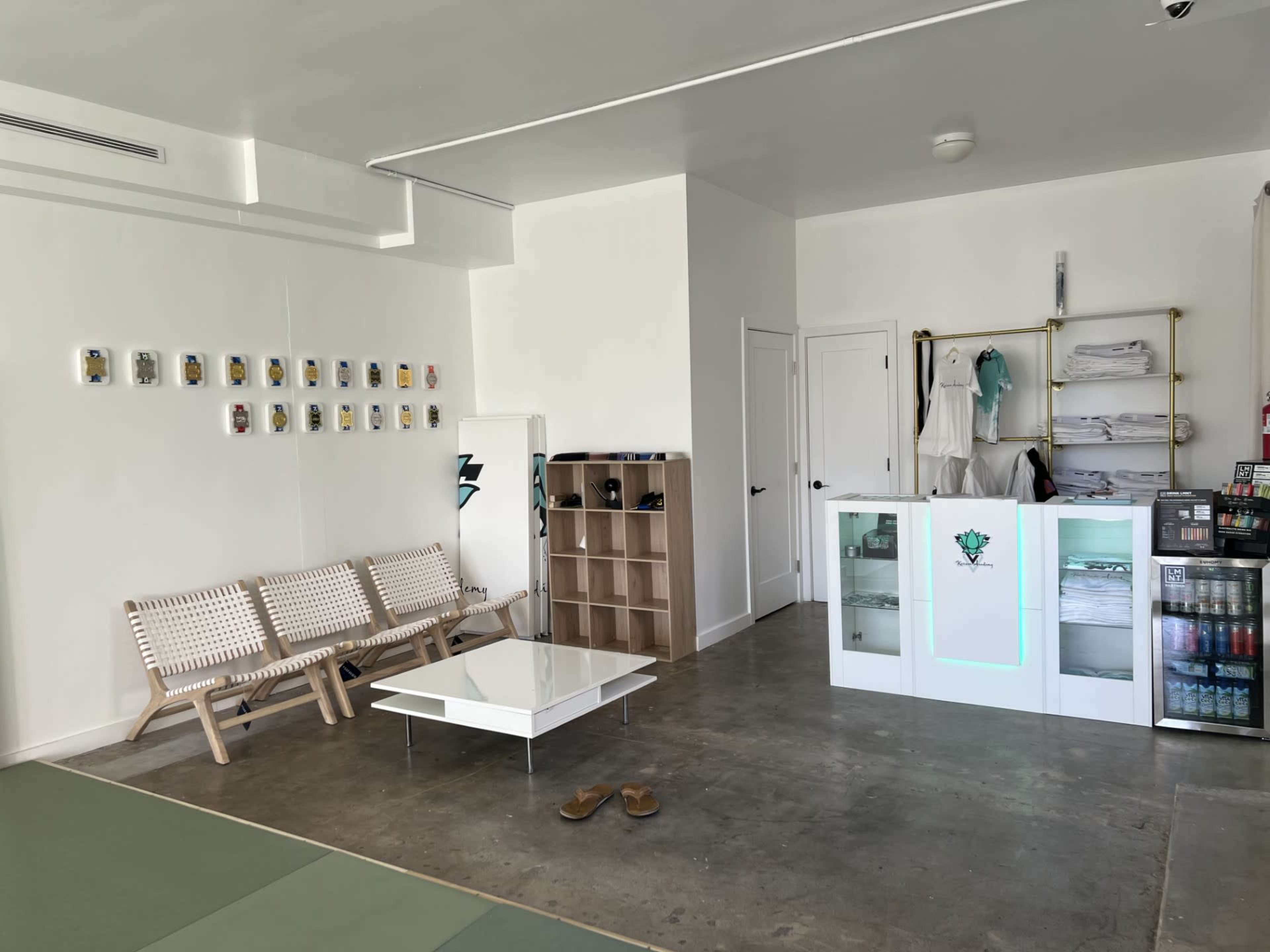 The image shows a modern, minimalist store interior with a seating area, a display counter, and a wall adorned with framed pictures.