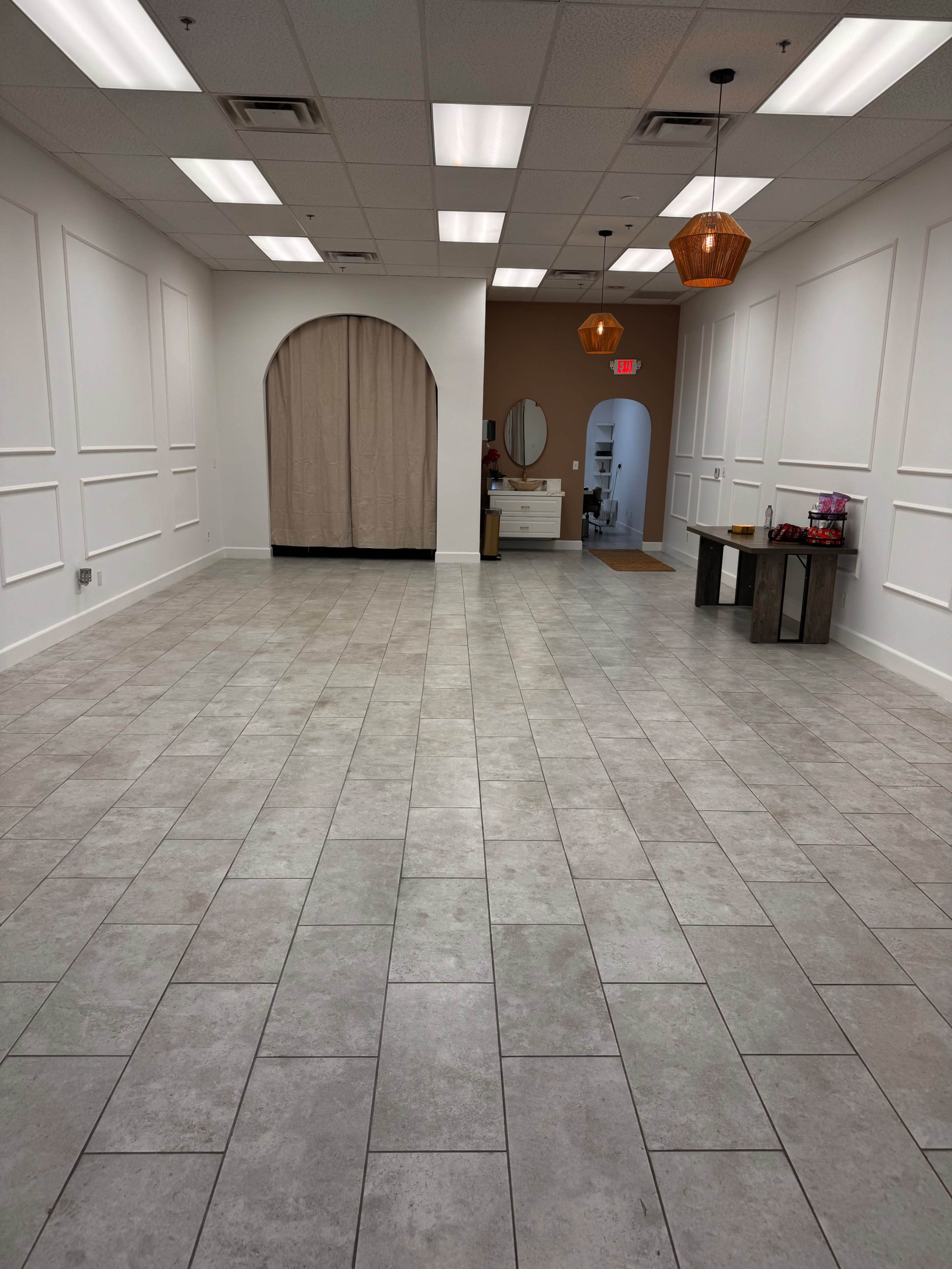 The image shows a large, empty interior space with tiled flooring, white walls, and decorative lighting fixtures.