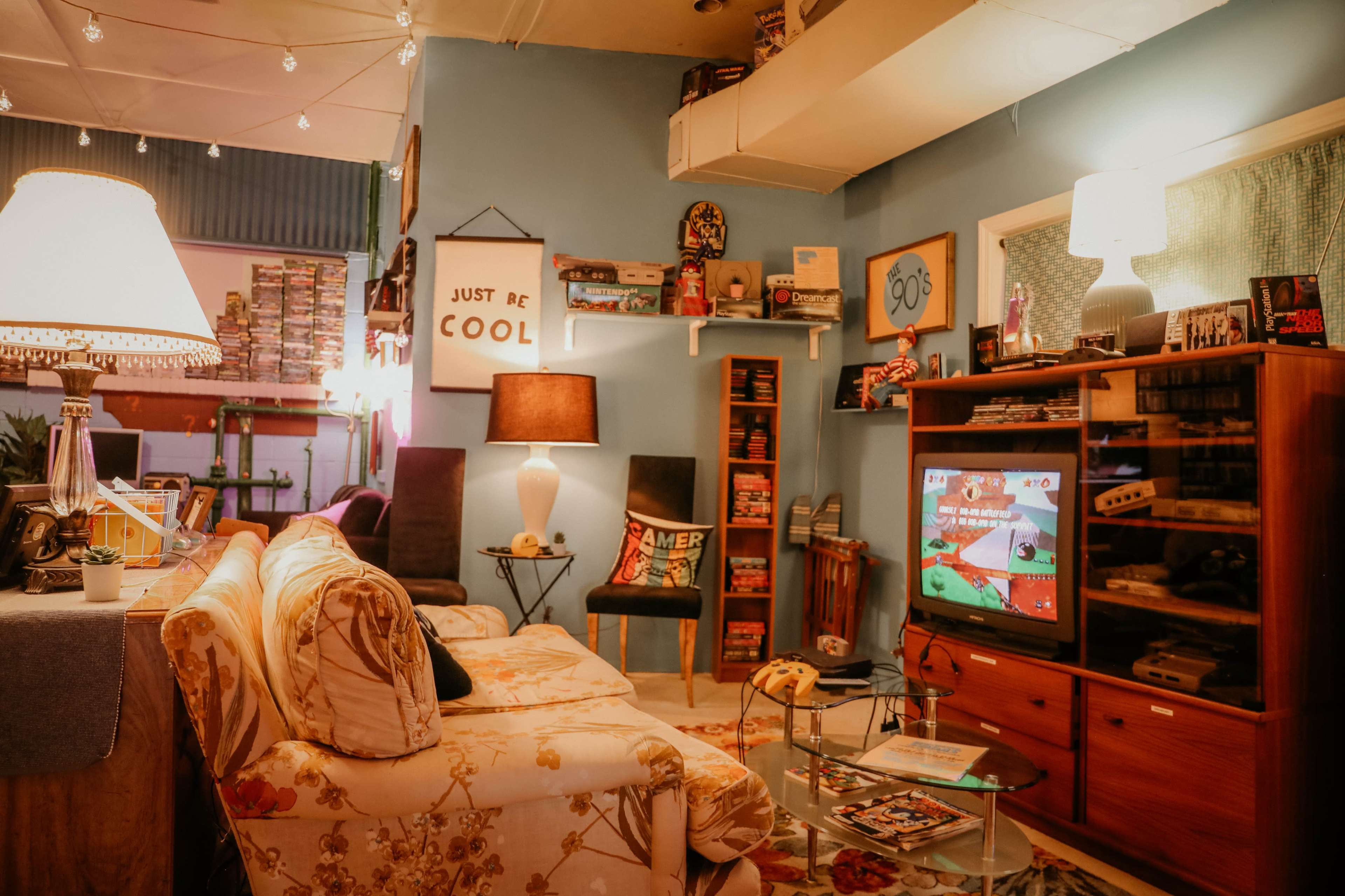 A cozy living room features a vintage television displaying a video game, surrounded by retro decor, a sofa, and shelves filled with games and collectibles.
